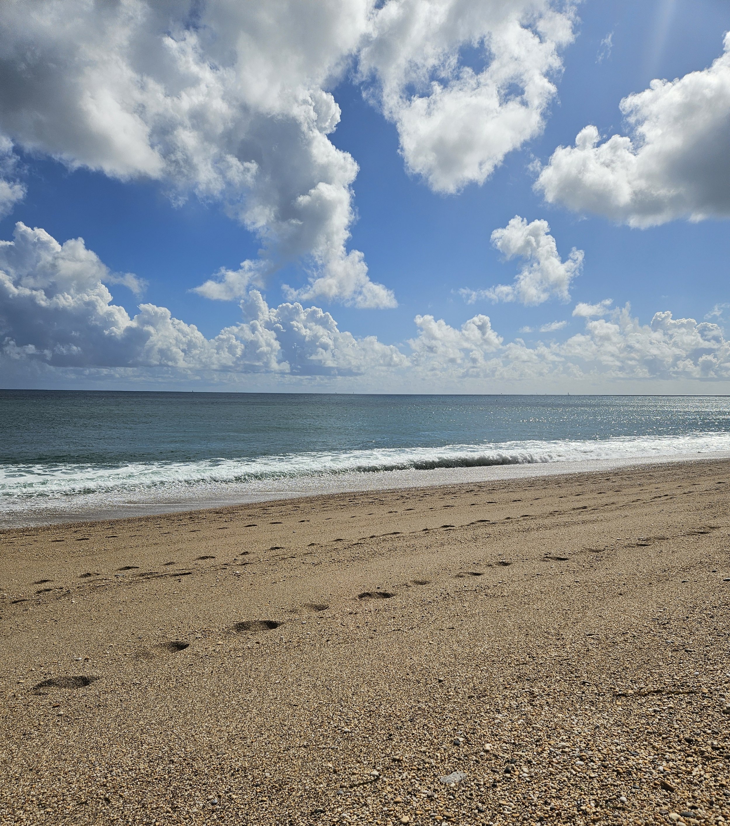 A sandy beach with footprints, calm ocean water, and a partly cloudy sky.