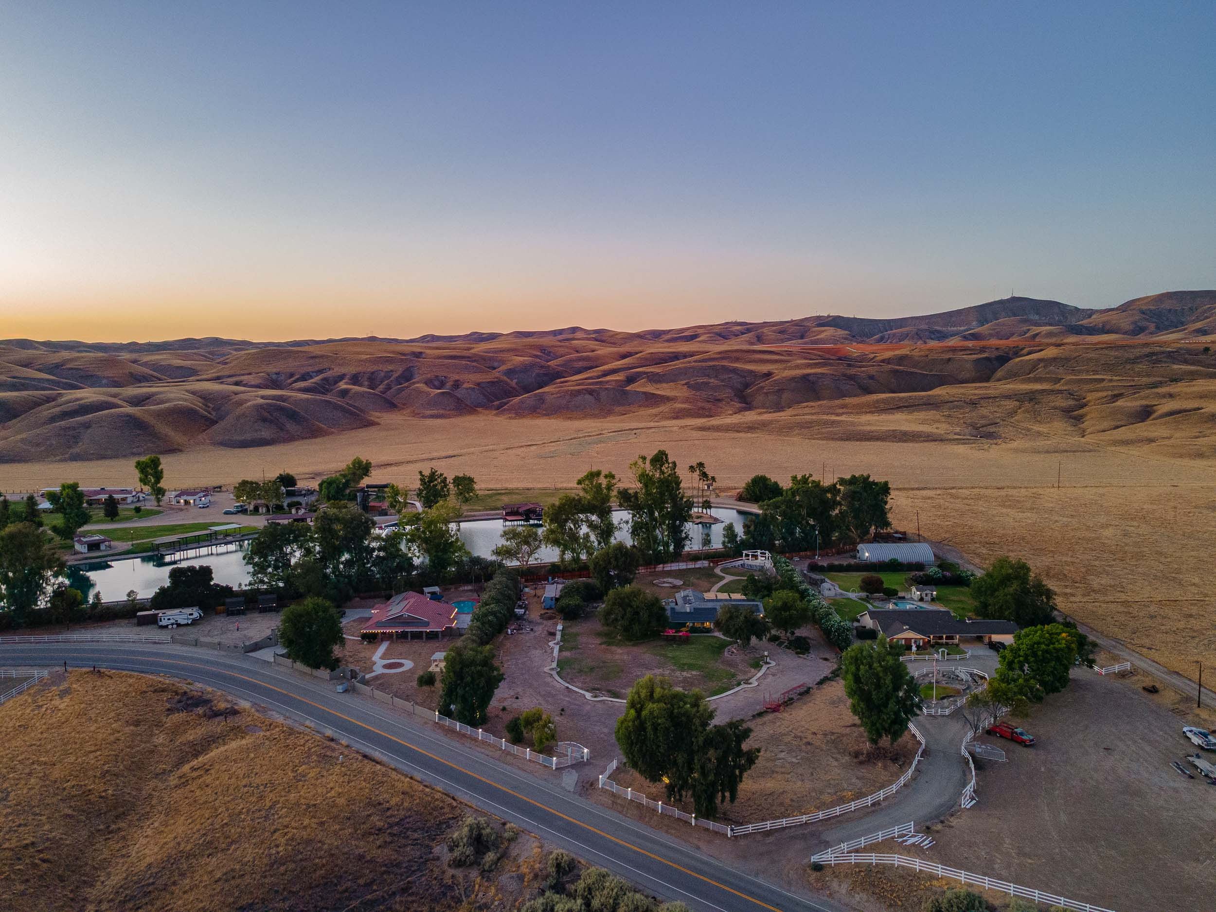 Aerial view of a residential farm with ponds, surrounded by rolling hills at sunset.