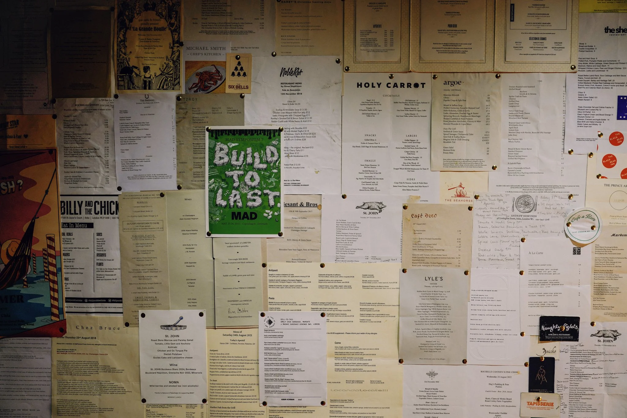 A wall covered with various restaurant menus and notices pinched with push pins.
