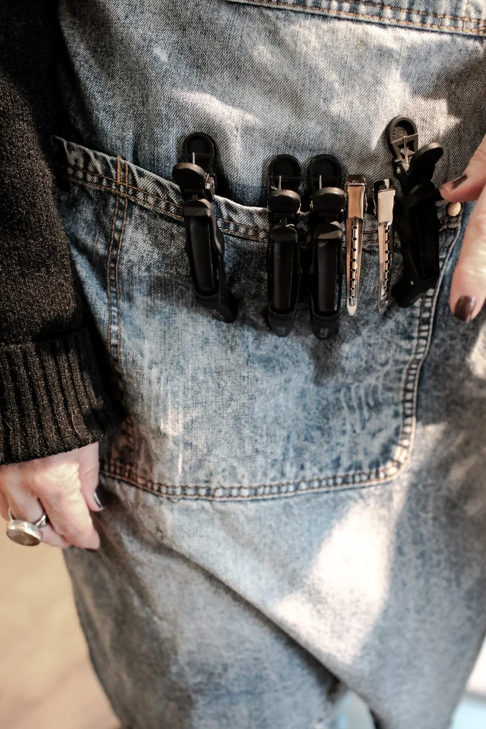 A person wearing blue jeans with four plastic clips and two metal clips attached to the front pocket.