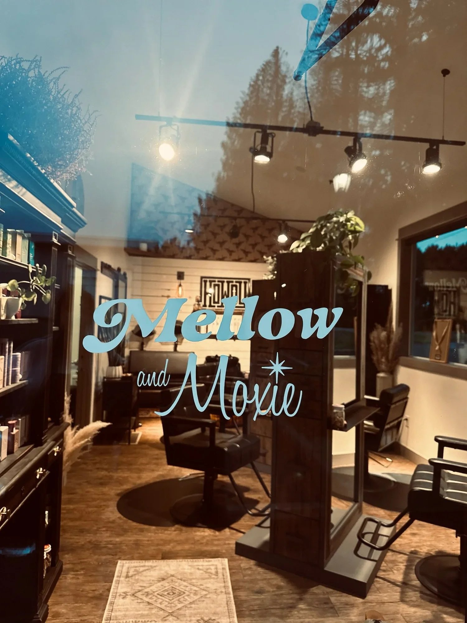The interior of a salon or studio with chairs, shelves, and decorative elements, visible through a glass door with the sign 'Mellow and Moxie' on it.