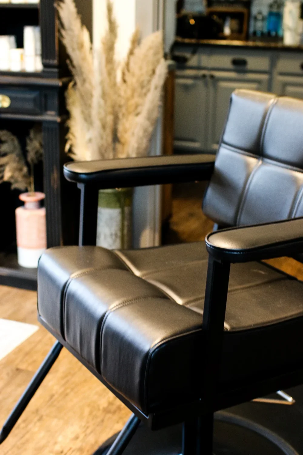 Close-up of a black modern leather lounge chair in a furniture store or showroom with a display cabinet and decorative dried pampas grass in the background.