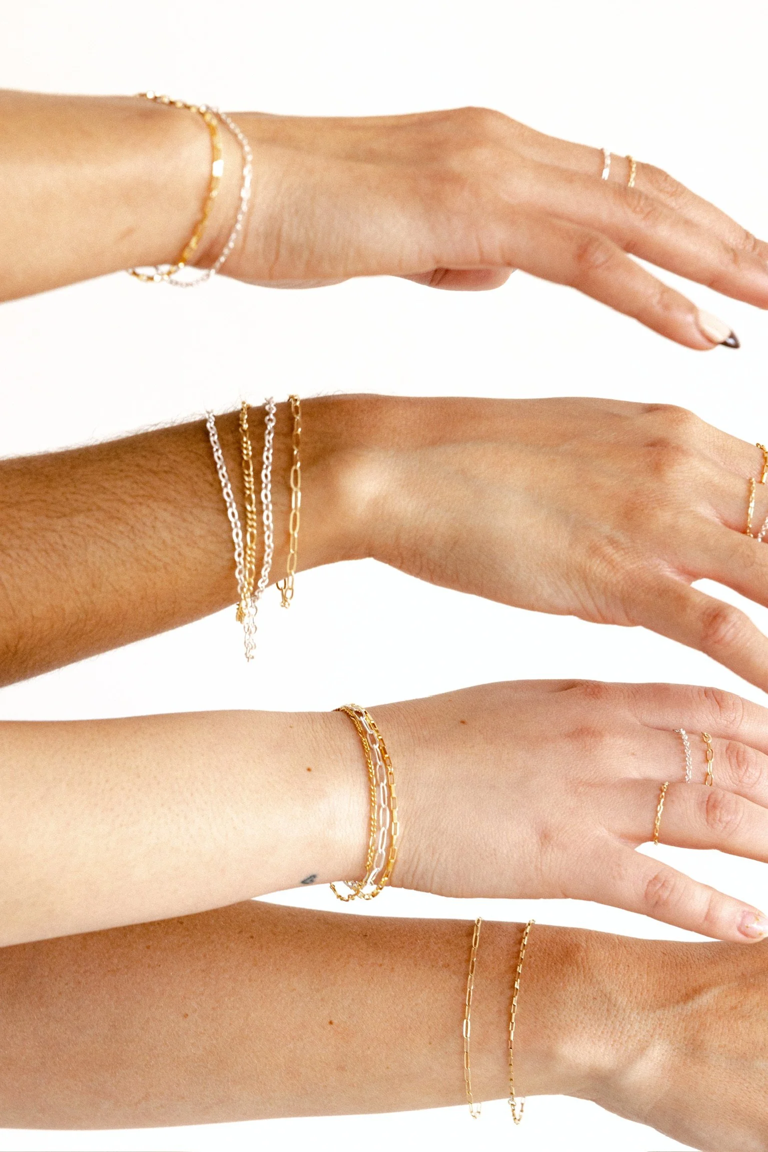 Multiple hands wearing gold and silver jewelry including bracelets and rings, arranged in a row against a white background.