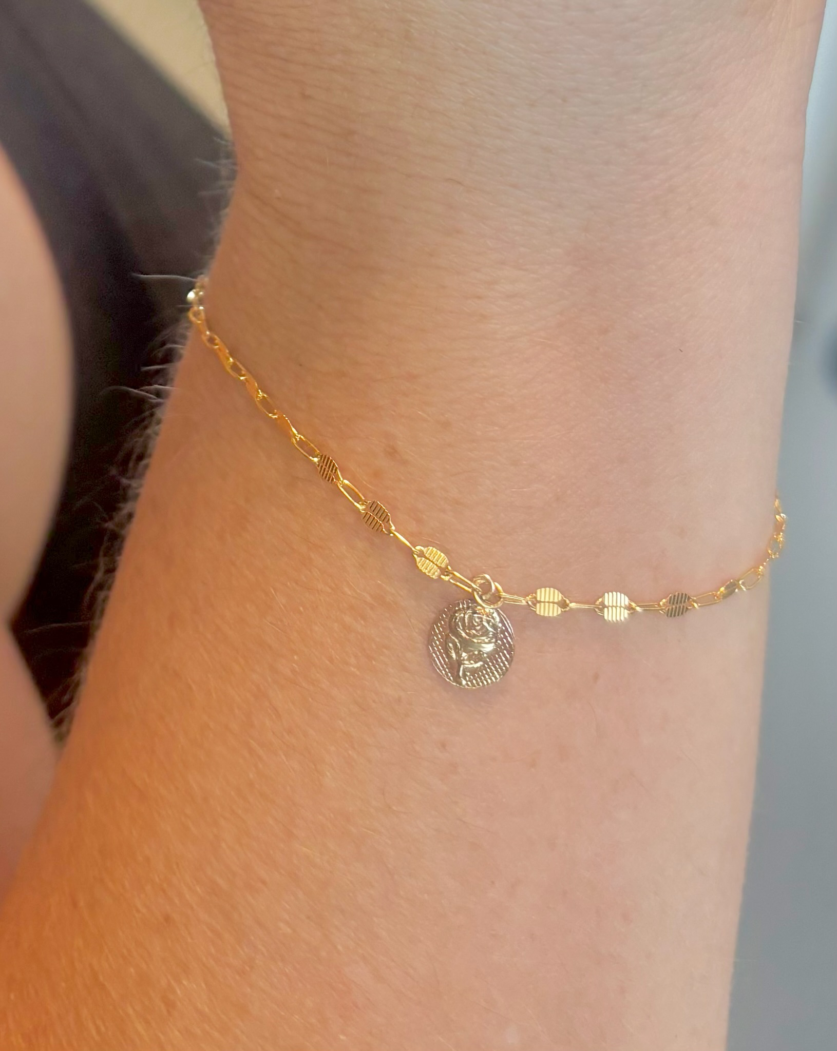 Close-up of a gold anklet with small circular charms, one of which has a design, worn around a person's ankle.