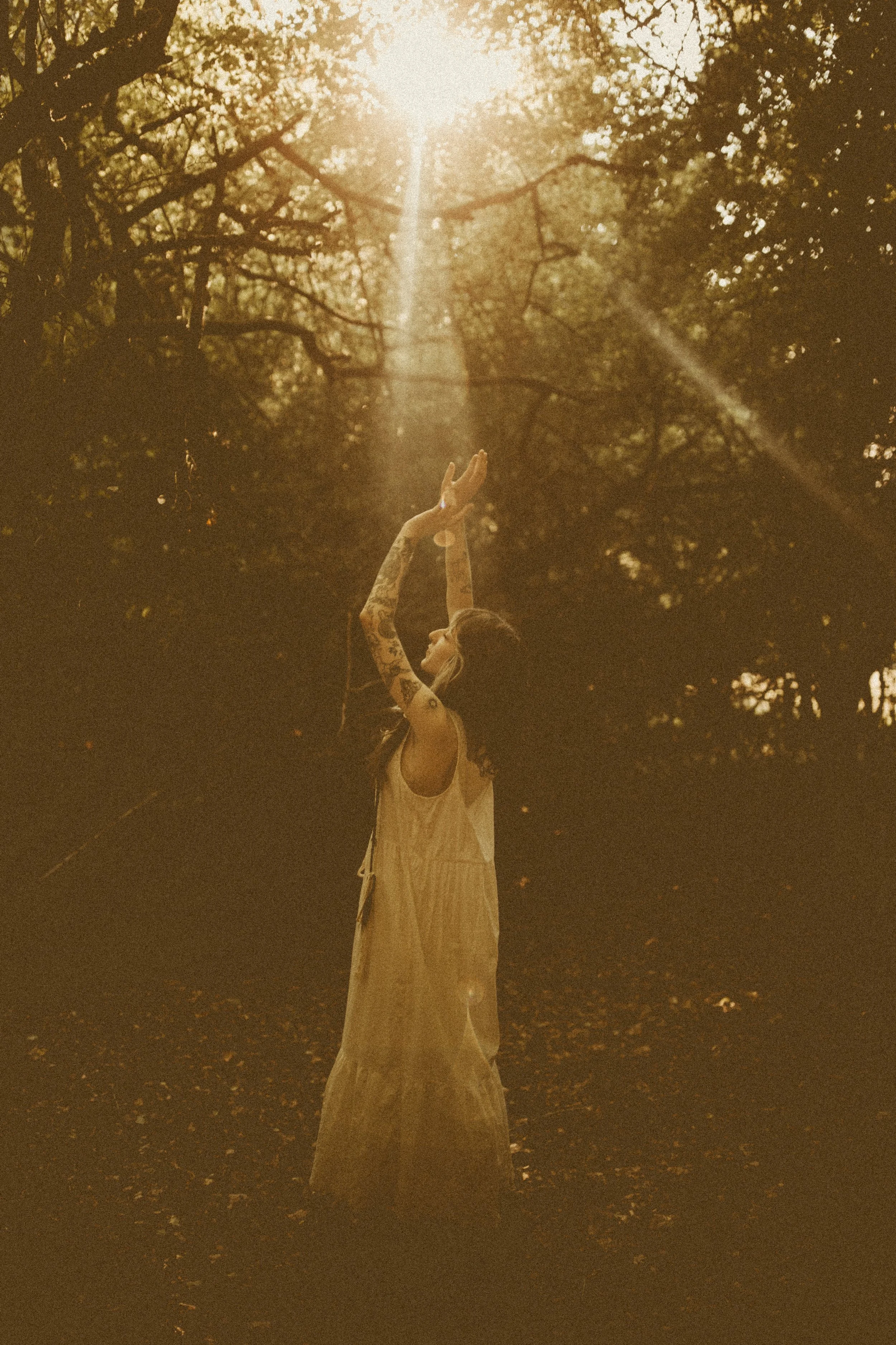 Woman standing in a forest reaching her arms toward sunlight filtering through trees