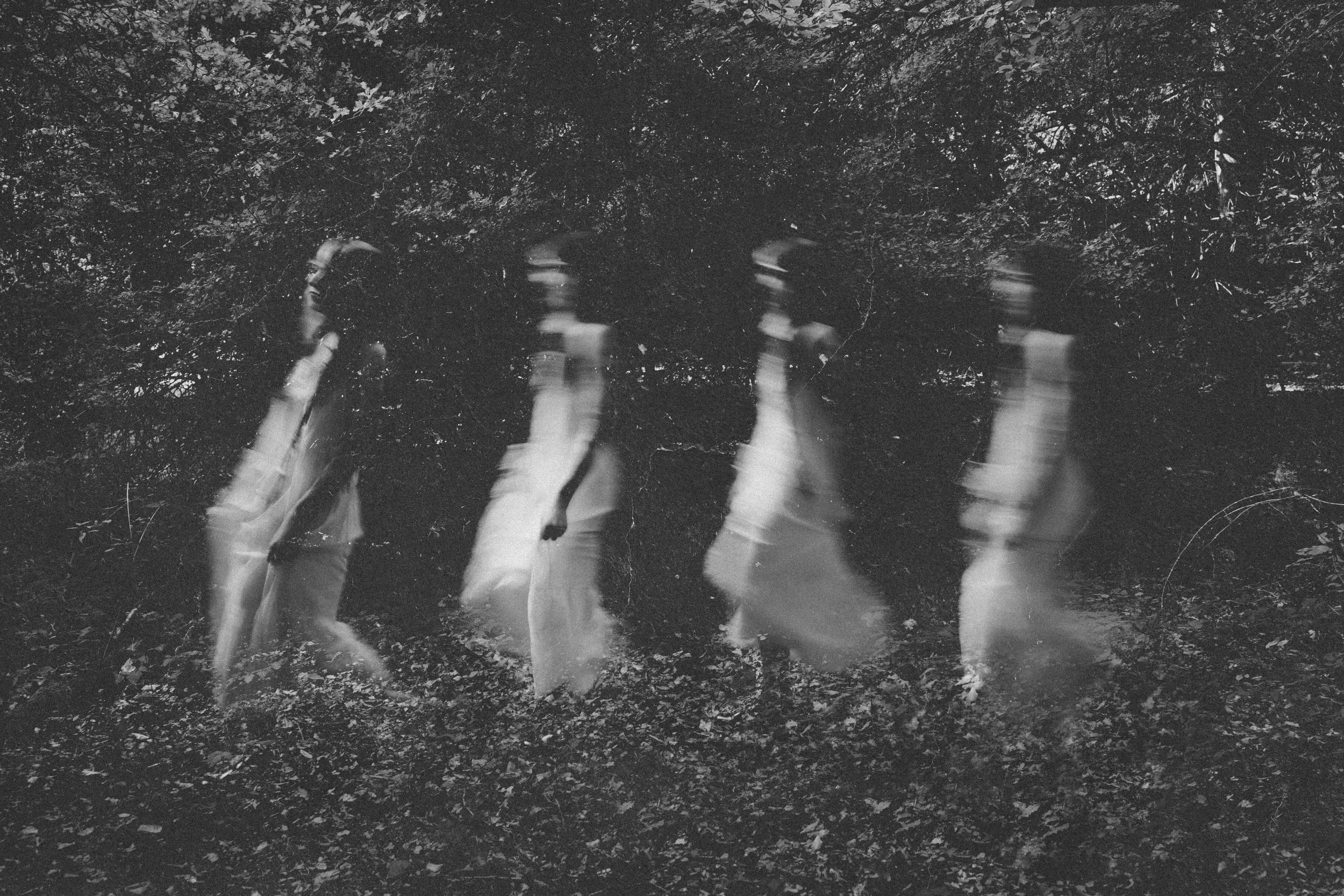 Blurred figures of witchy women in flowing white garments walking through a forest