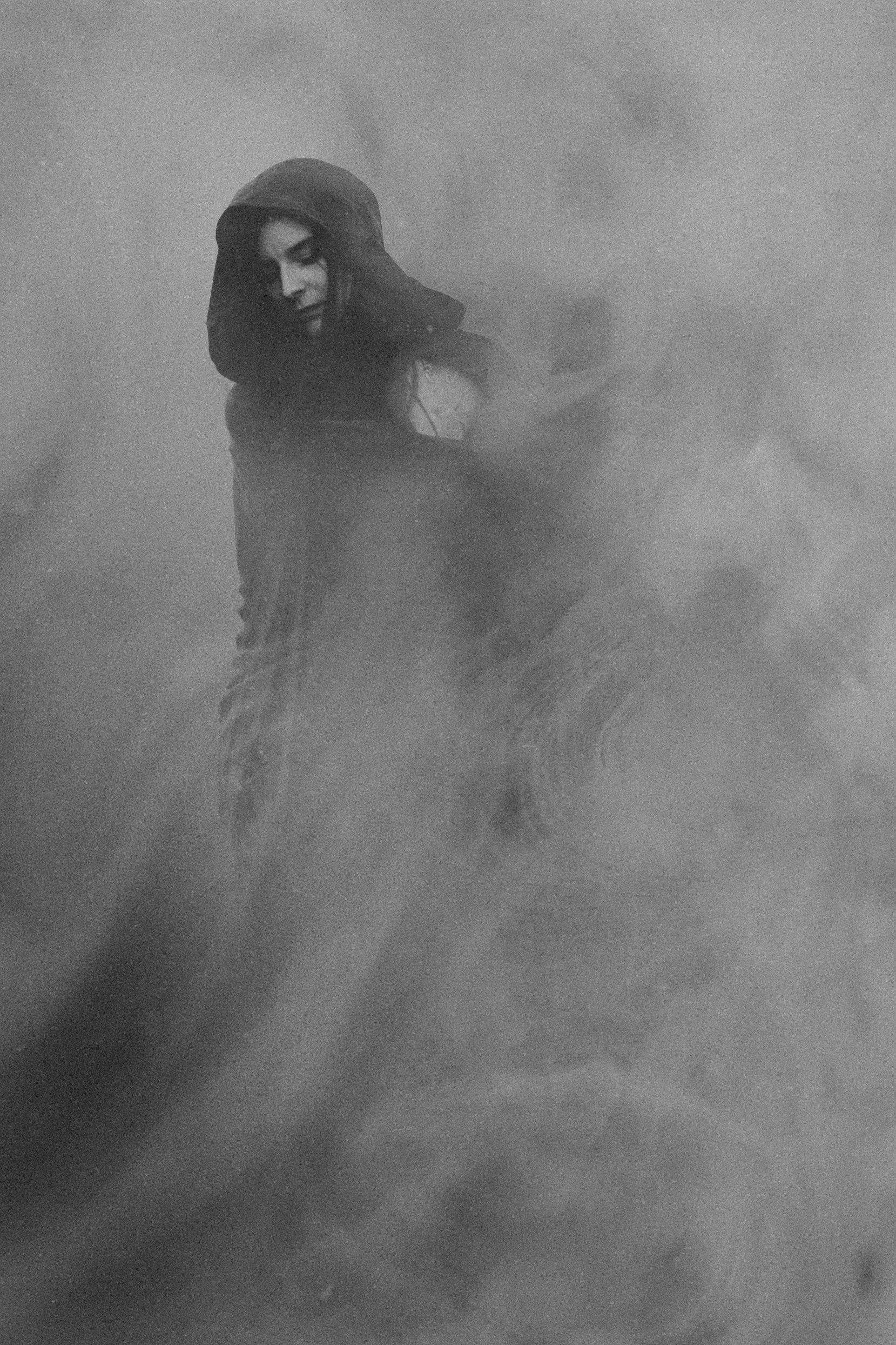 Black-and-white image of a hooded woman standing in mist