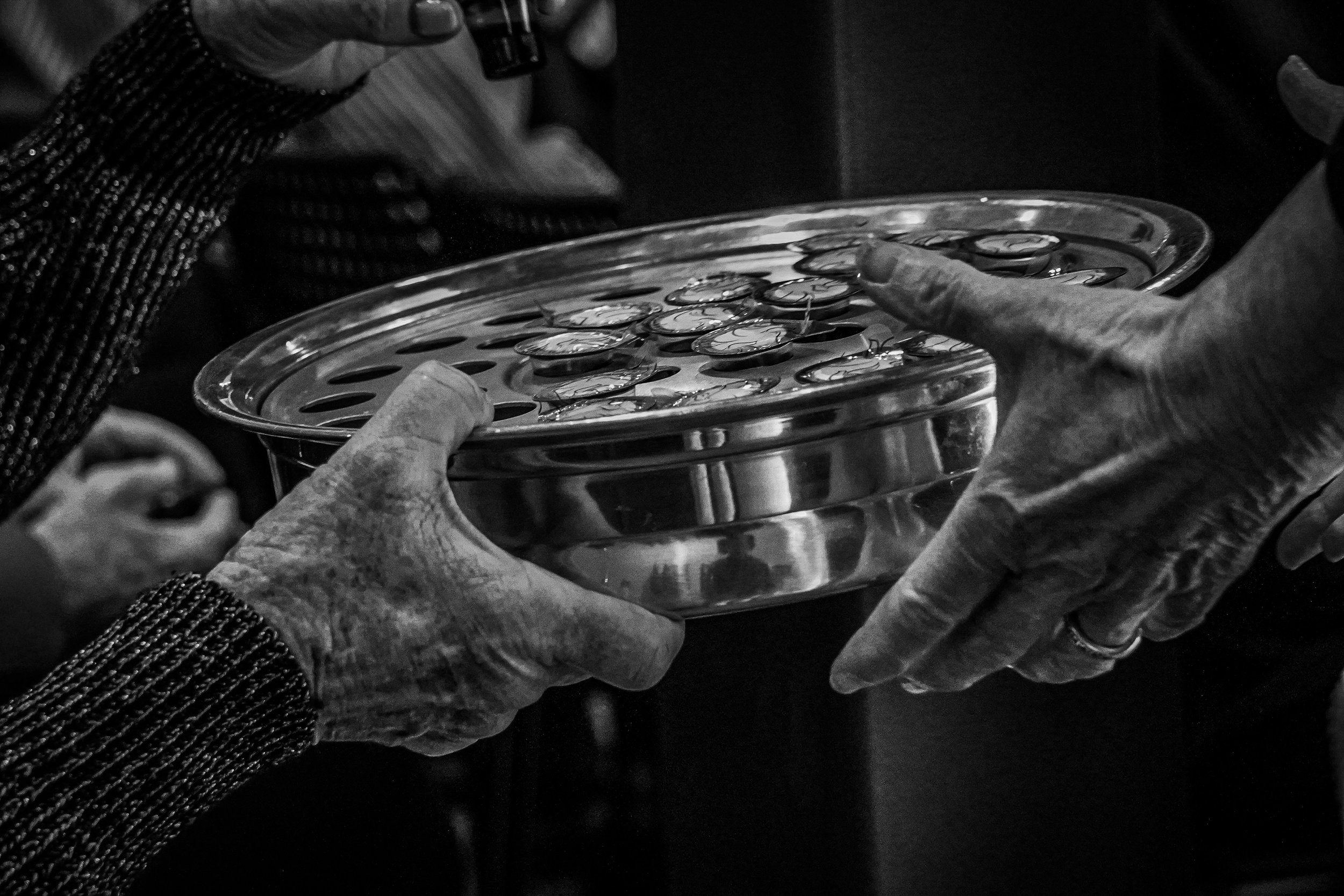 Two elderly hands exchanging a glass dish with small circular objects inside.