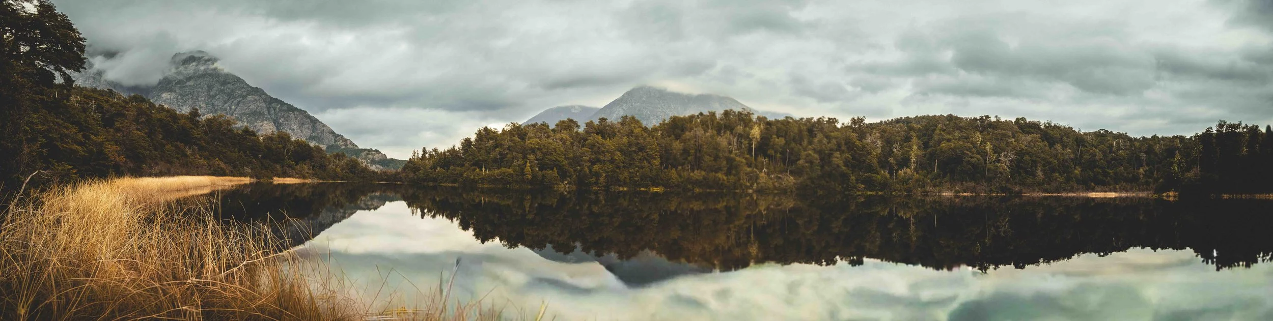 Paisaje de montañas y árboles reflejados en un lago en un día nublado