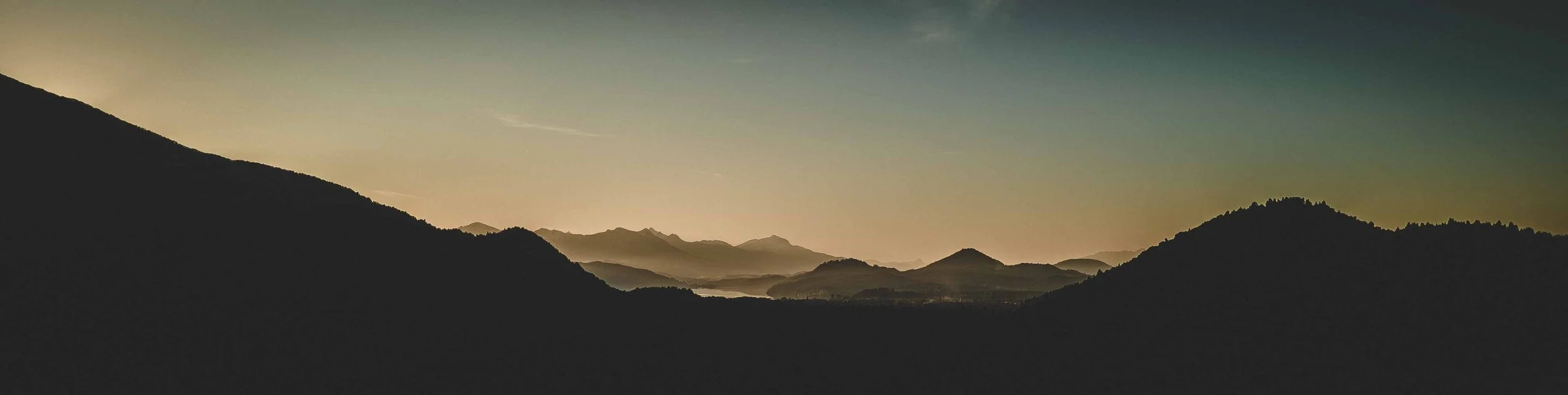 Paisaje de montañas al atardecer con cielo despejado y suaves colores cálidos.