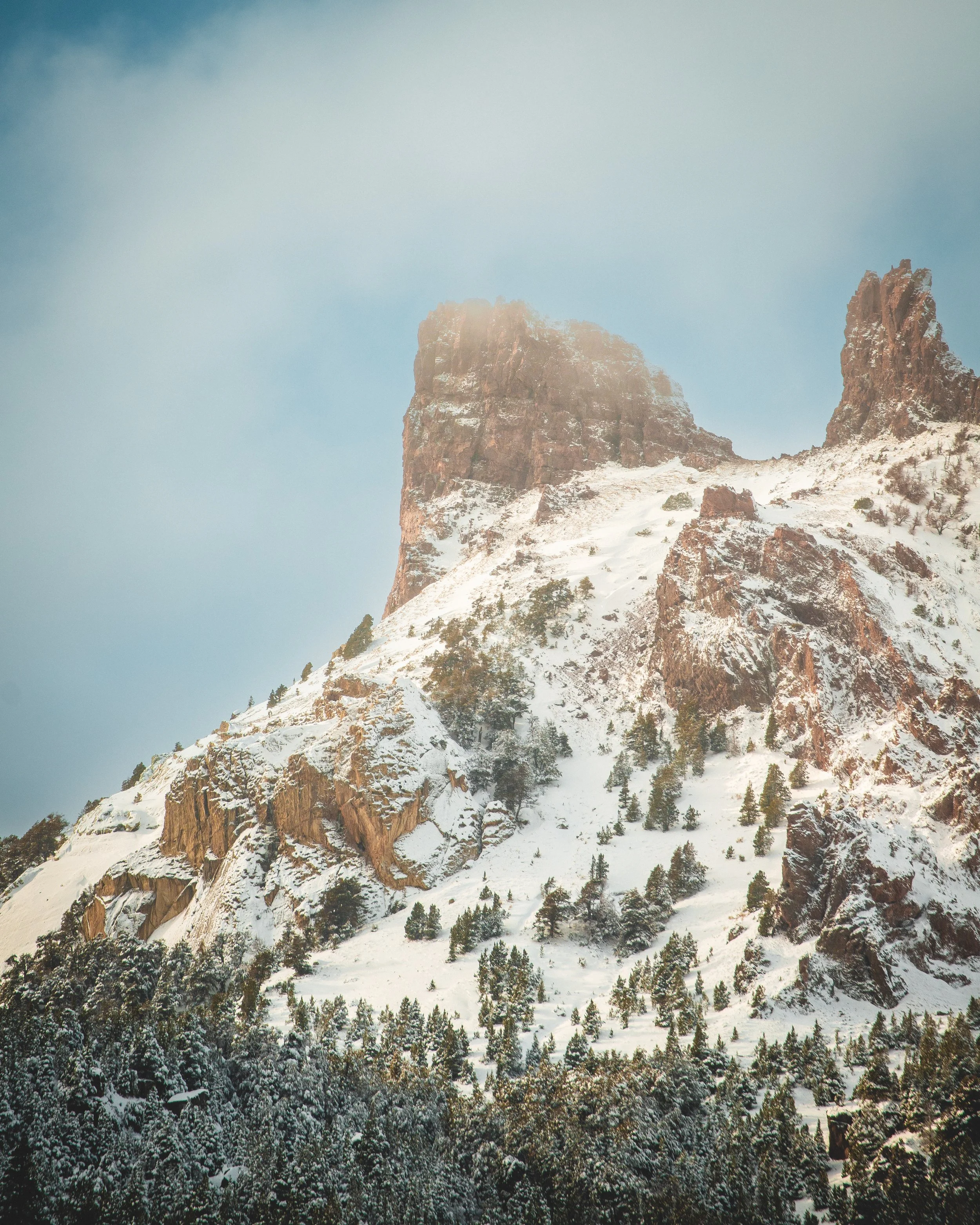 Montaña nevada con pinos y rocas rojas.