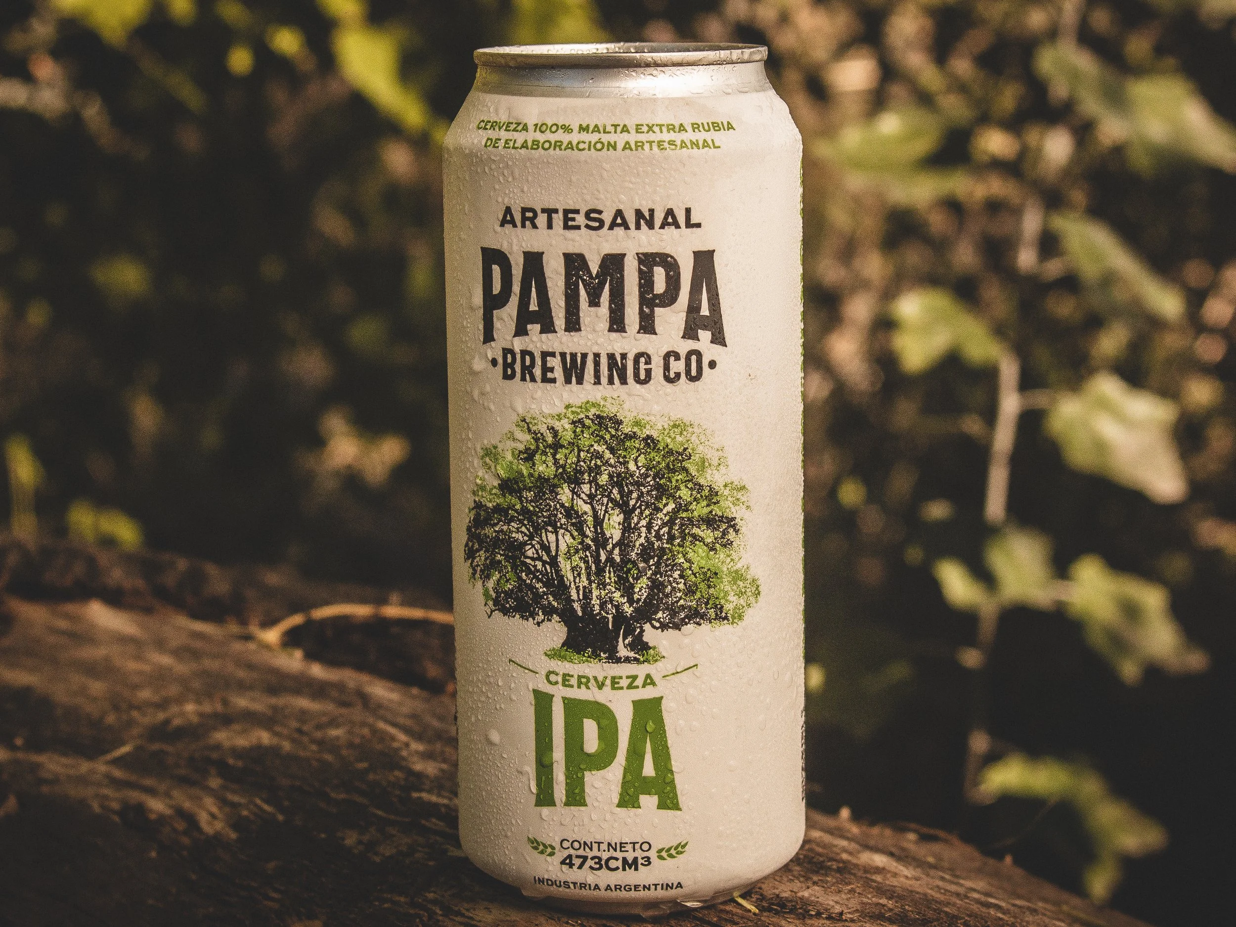 Lata de cerveza artesanal Pampa Brewing Co IPA en un entorno natural con fondo de hojas verdes y árbol impreso en la lata.