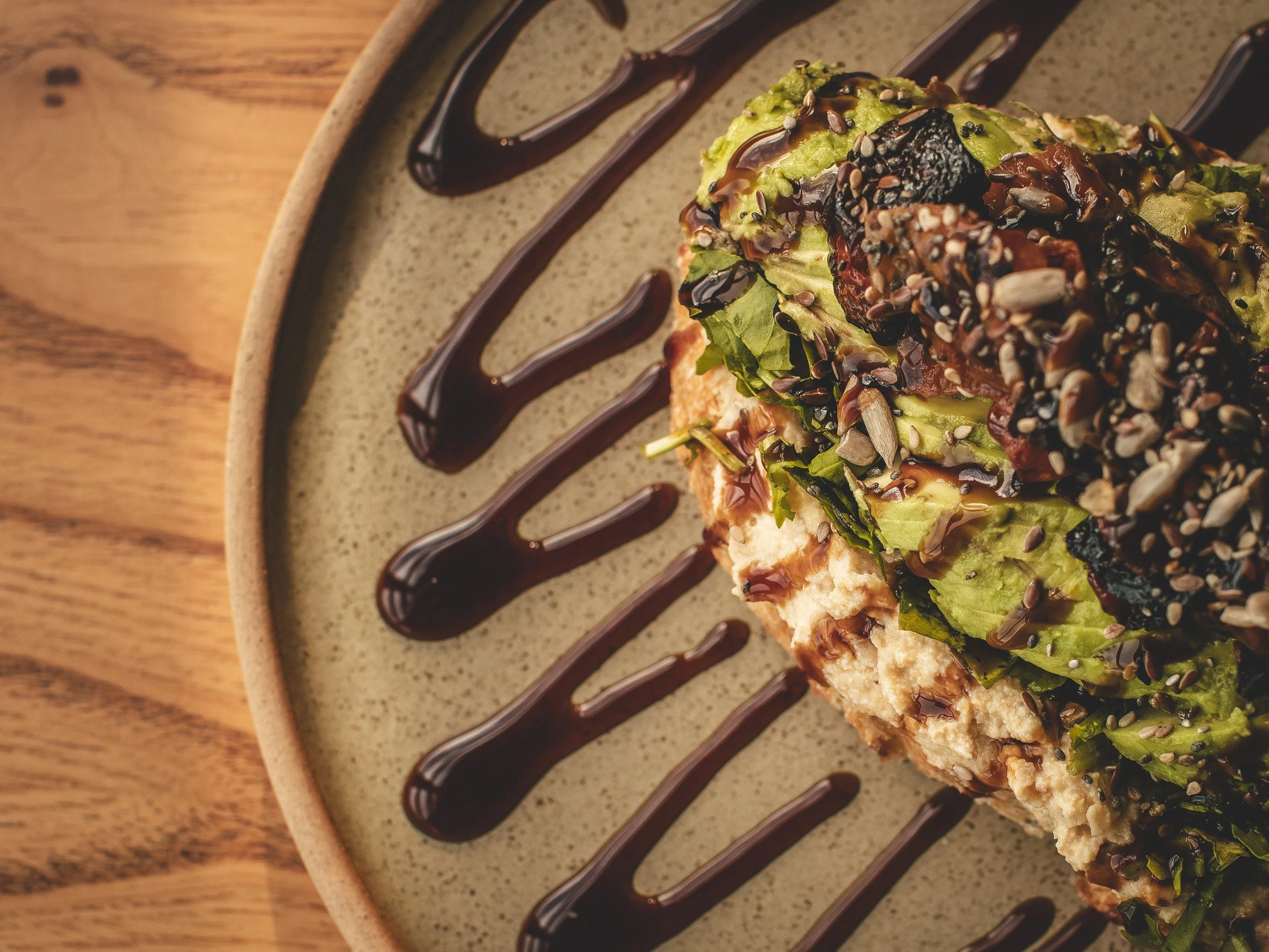 Ensalada con aguacate, semillas y aderezo en plato con salsa de chocolate, sobre mesa de madera.