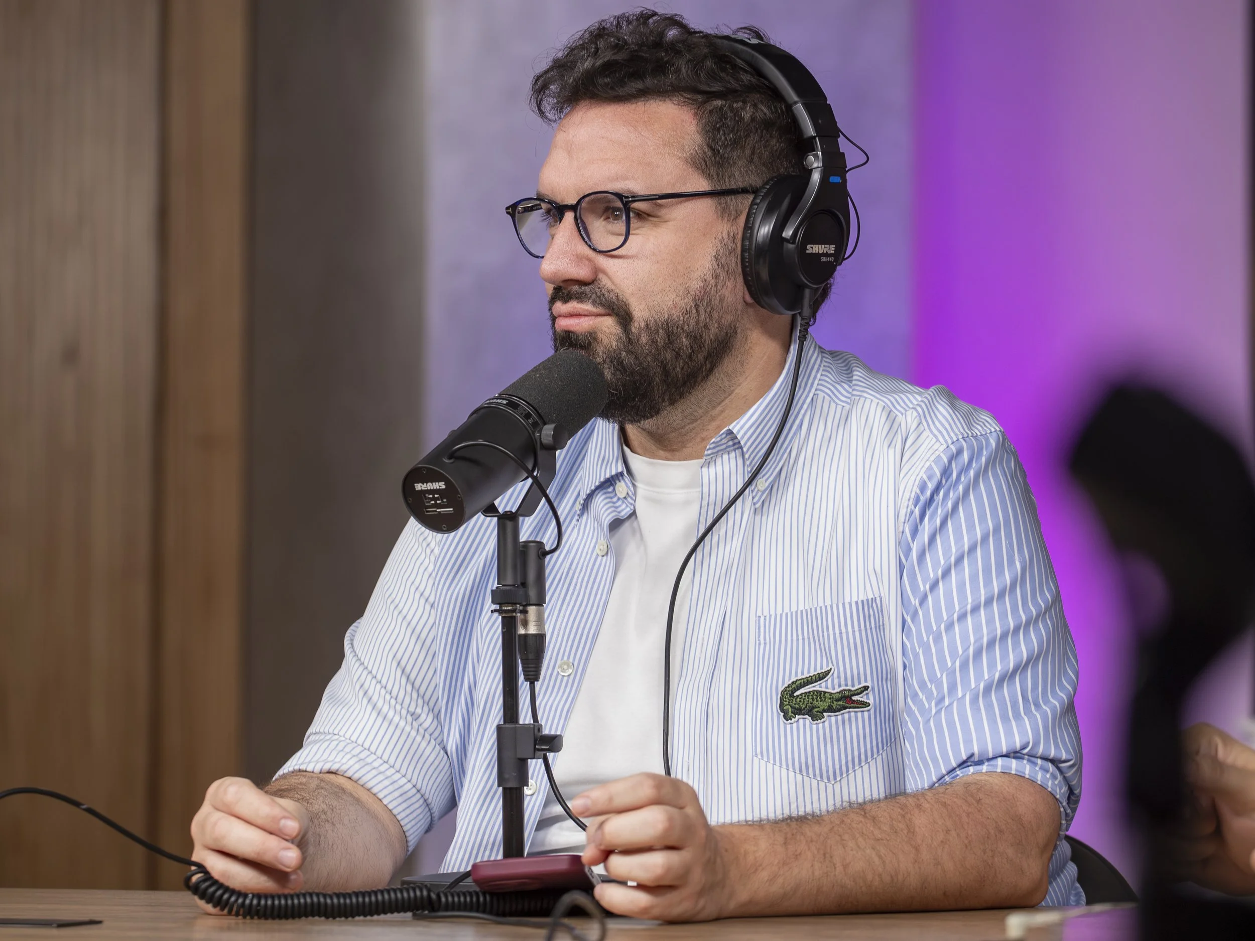 Hombre con barba y gafas, usando auriculares y frente a un micrófono en un estudio de grabación.