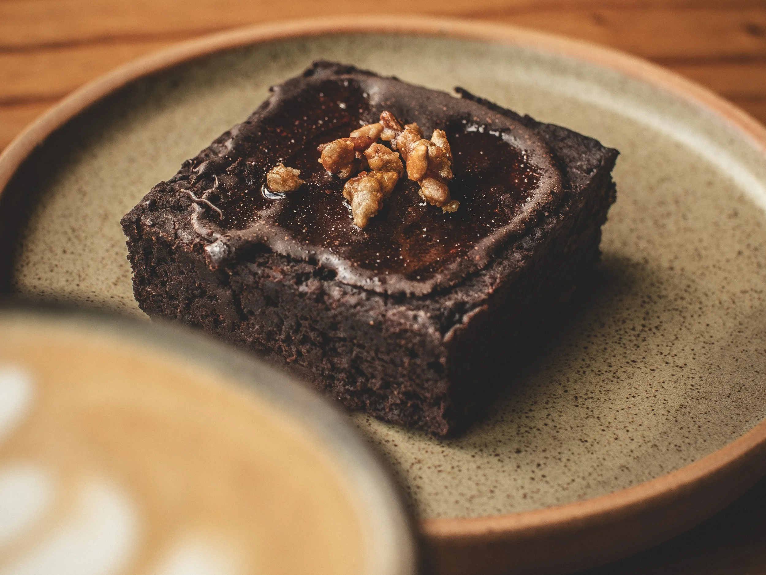 Cuadrado de pastel de chocolate cubierto con glaseado de chocolate y decorado con nueces en la parte superior, servido en un plato de cerámica beige.