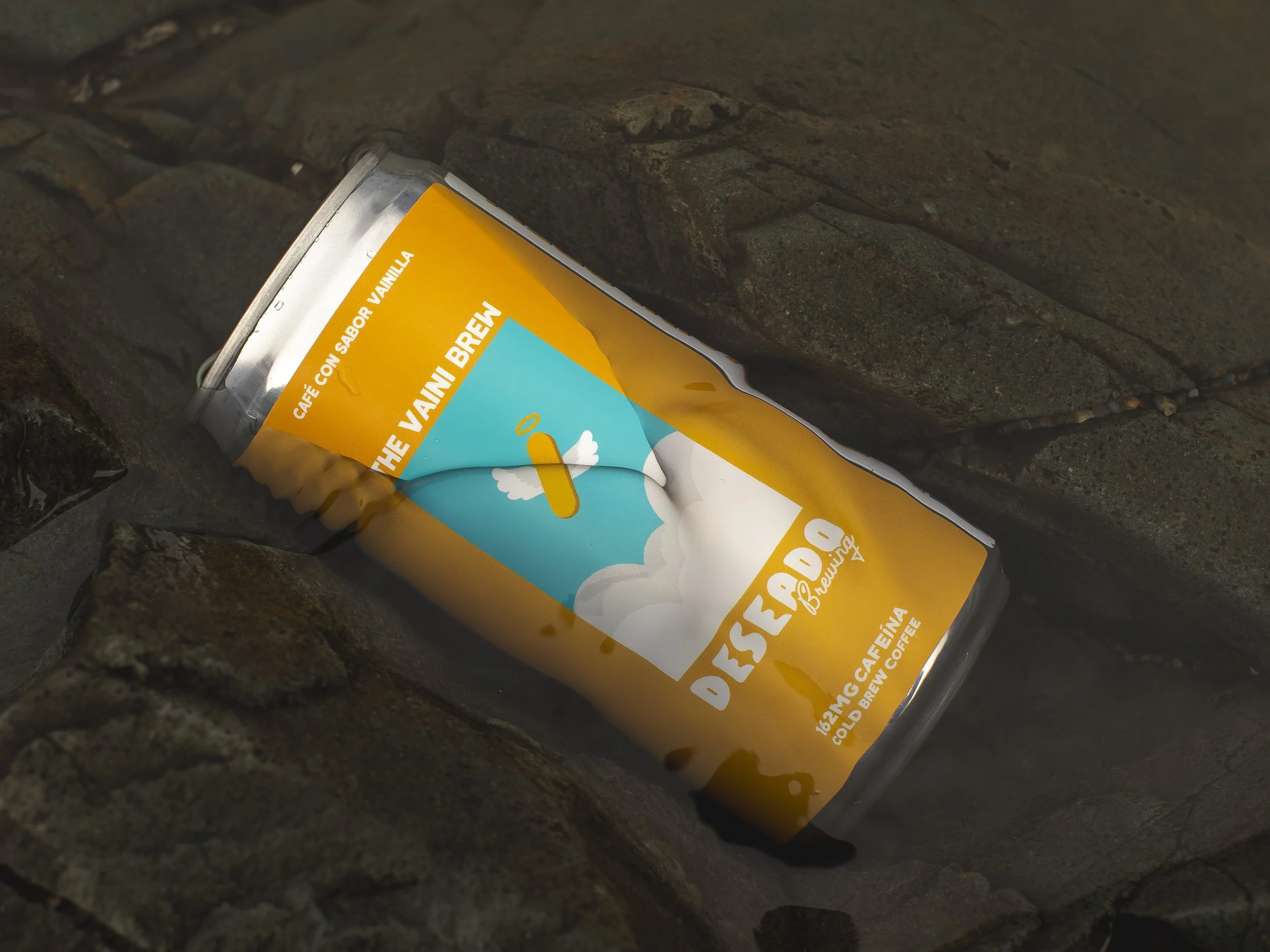 Lata de café Descafeinado Brew en un patio de piedras, con etiqueta amarilla y azul que muestra un dibujo de una nube y un avión. La lata está sobre piedras.