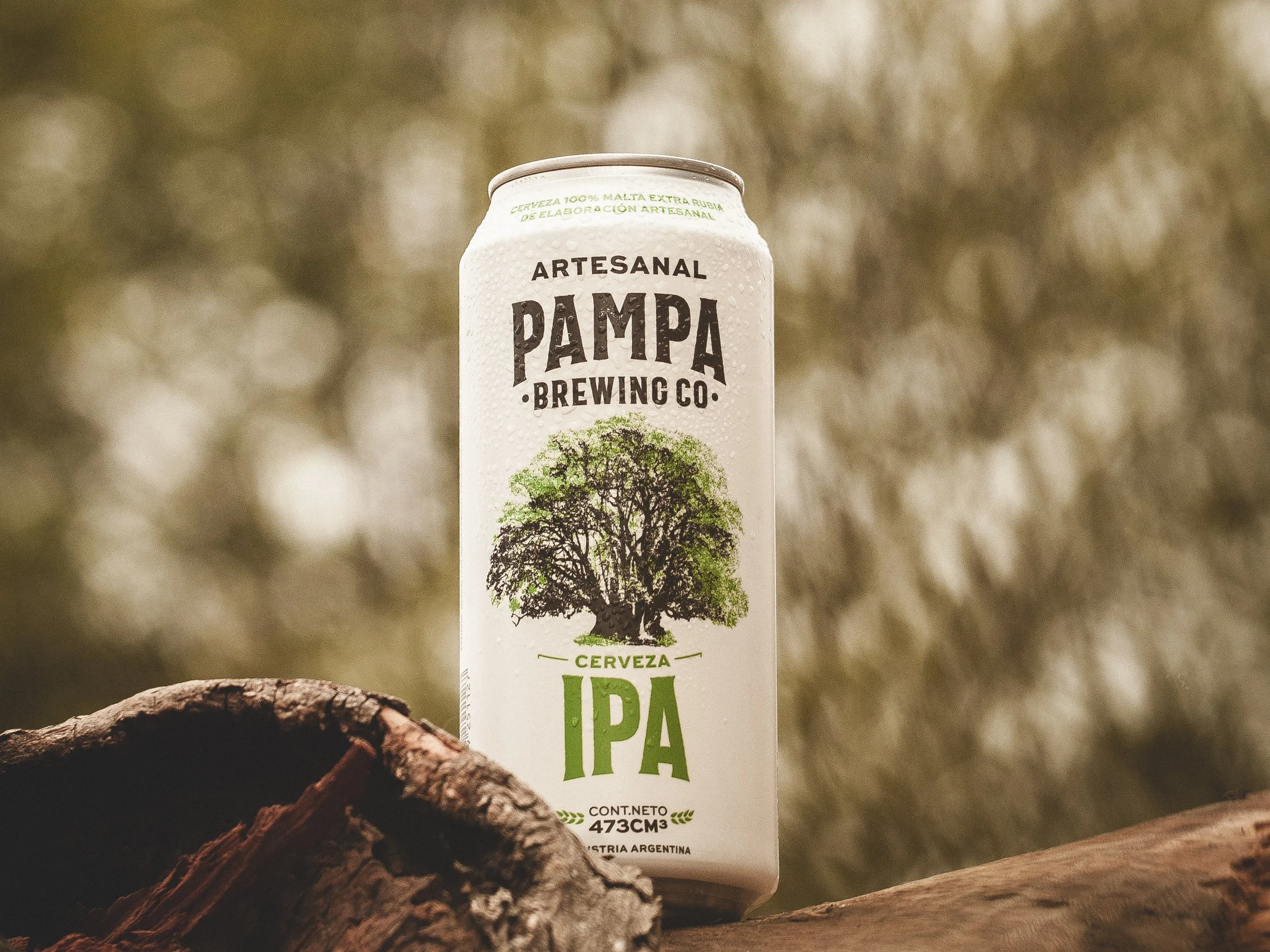 Lata de cerveza artesanal Pampa Brewing Co. IPA con borde de agua y fondo de naturaleza difuso.