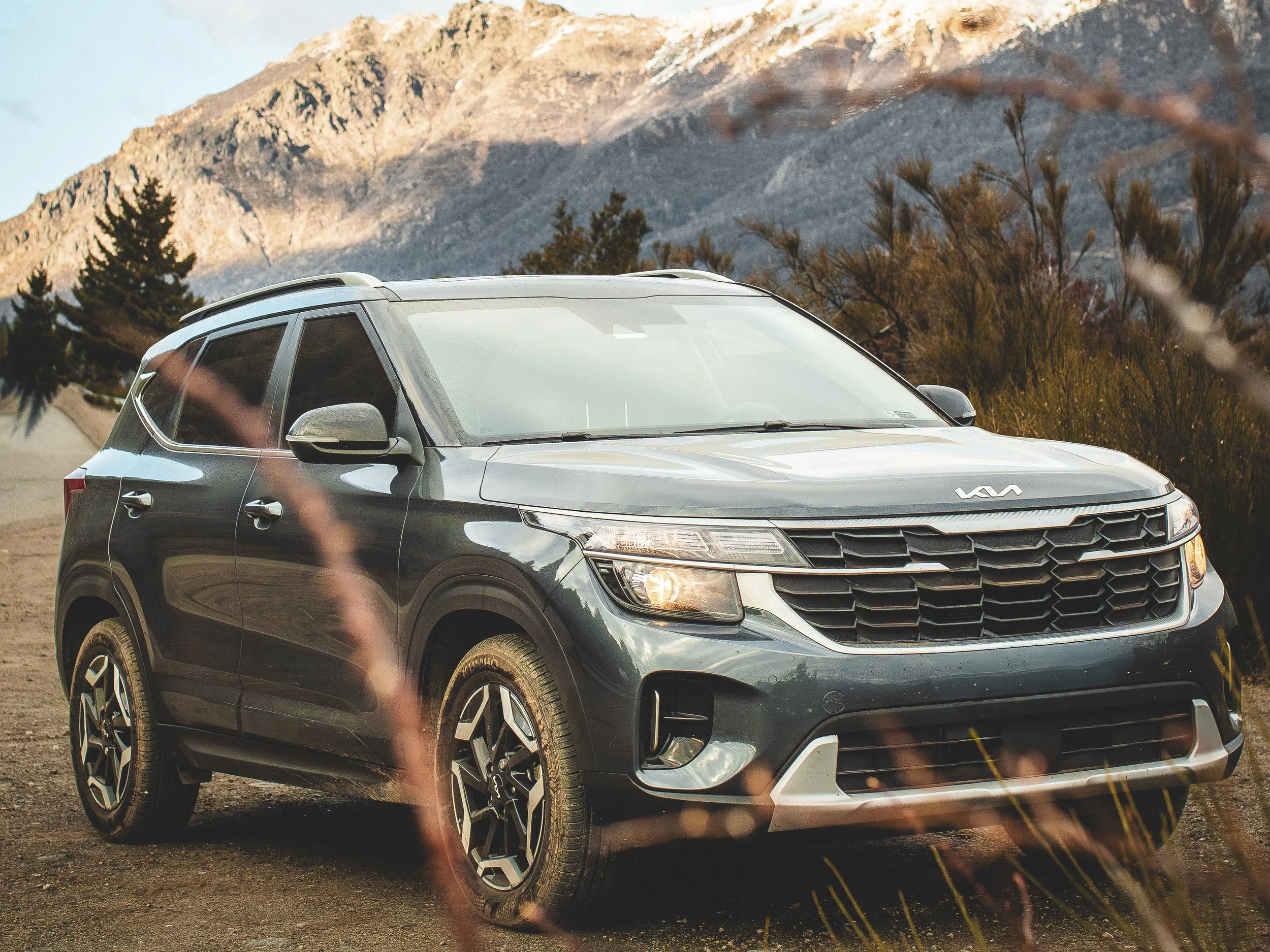 Automóvil Kia SUV en entorno montañoso con vegetación y sendero de tierra