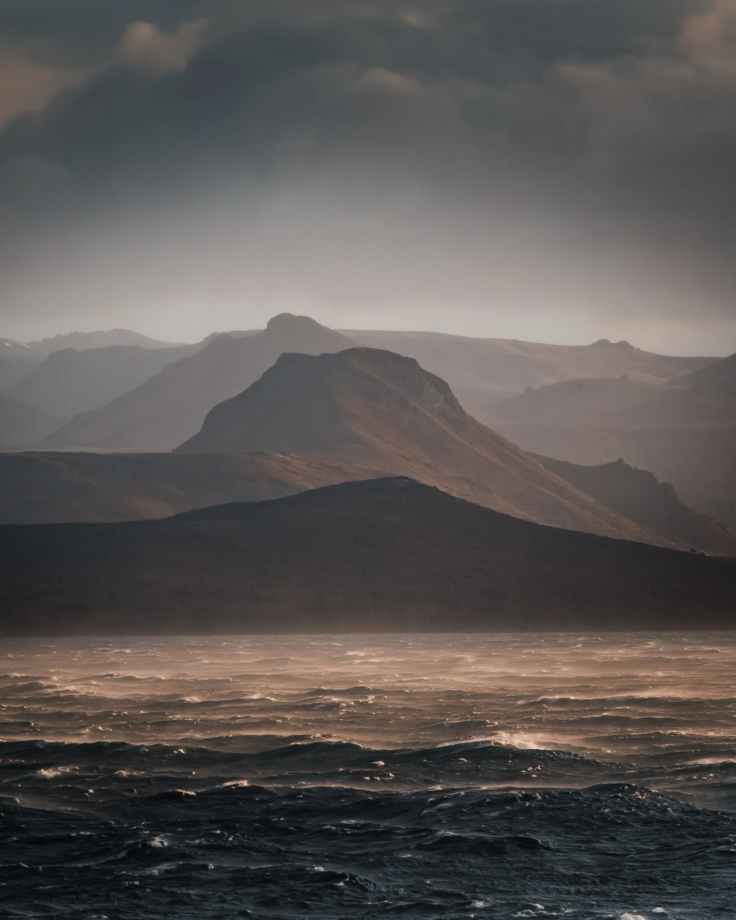 Olas en el mar frente a montañas nubladas en un día nublado.
