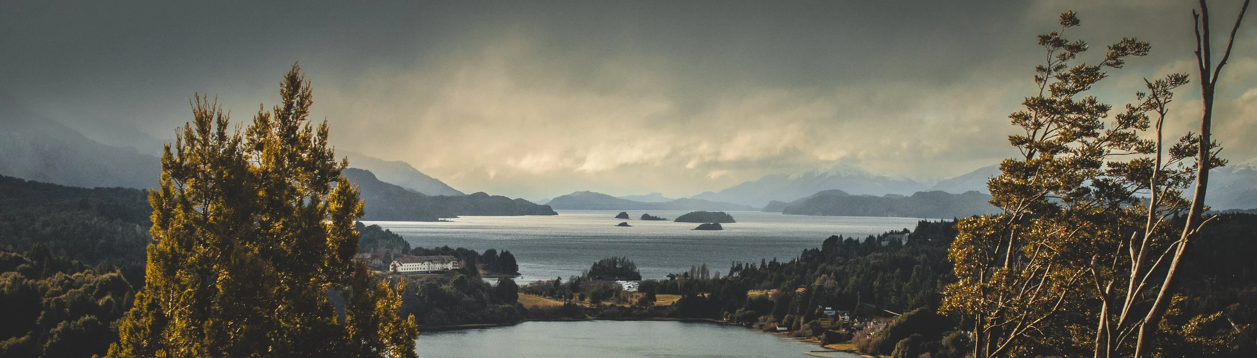 Paisaje con lagos, árboles y montañas en la distancia en un día nublado.