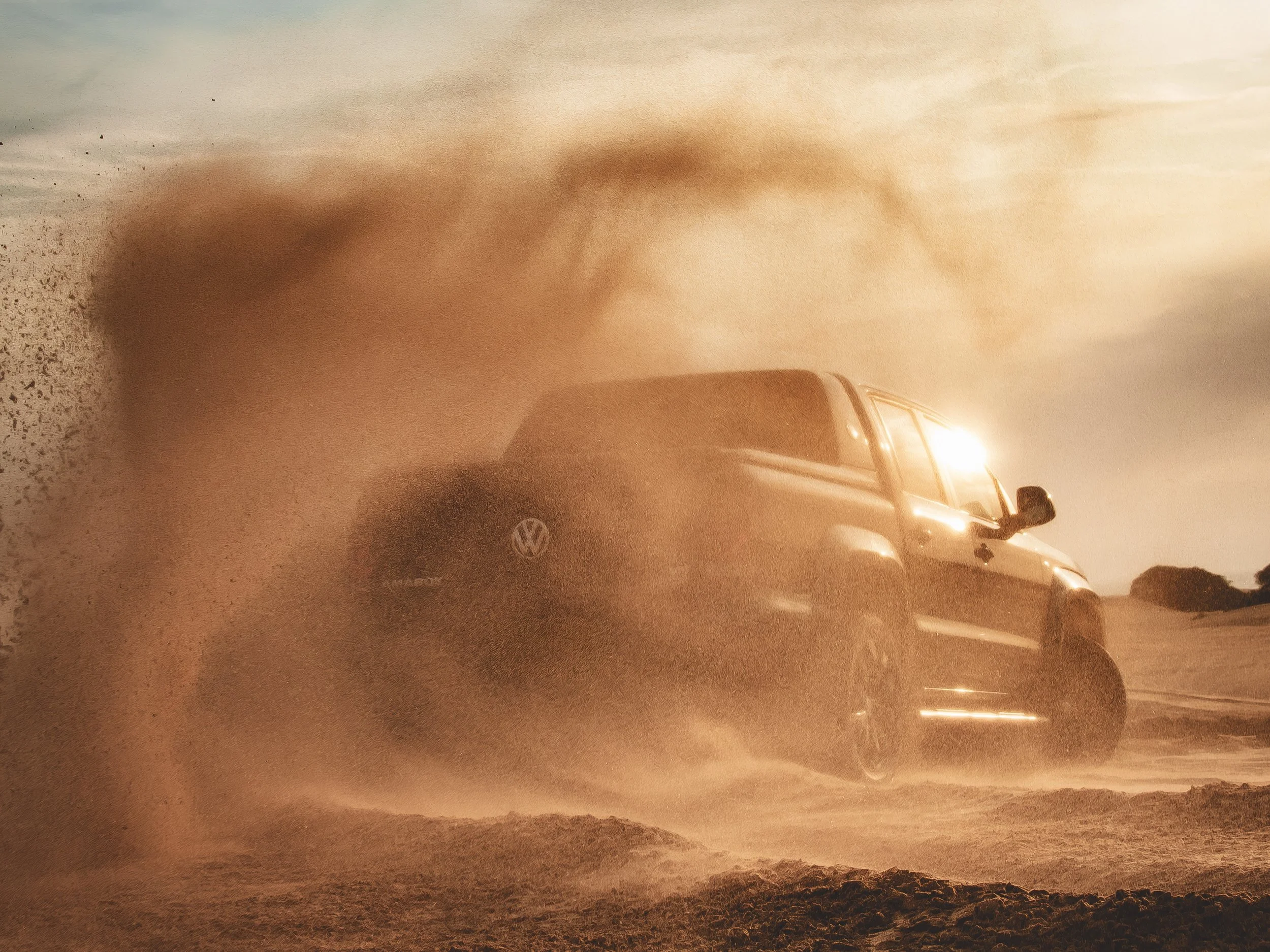 Un automóvil Volkswagen Taro conduciendo a través de una tierra arenosa y despejada durante el atardecer, creando una nube de polvo detrás.