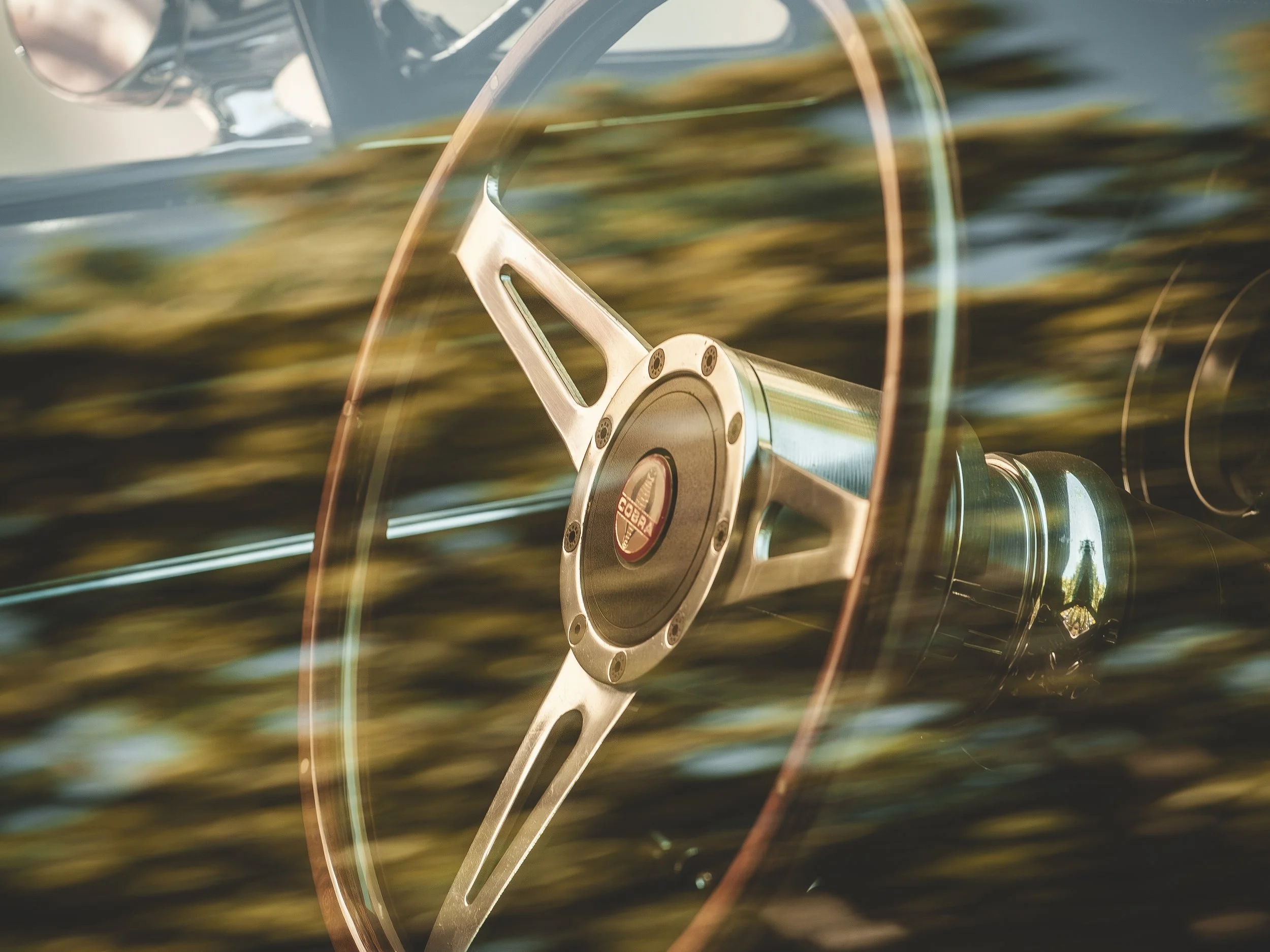 Volante de un coche clásico con fondo de árboles y naturaleza, vista desde dentro del vehículo.