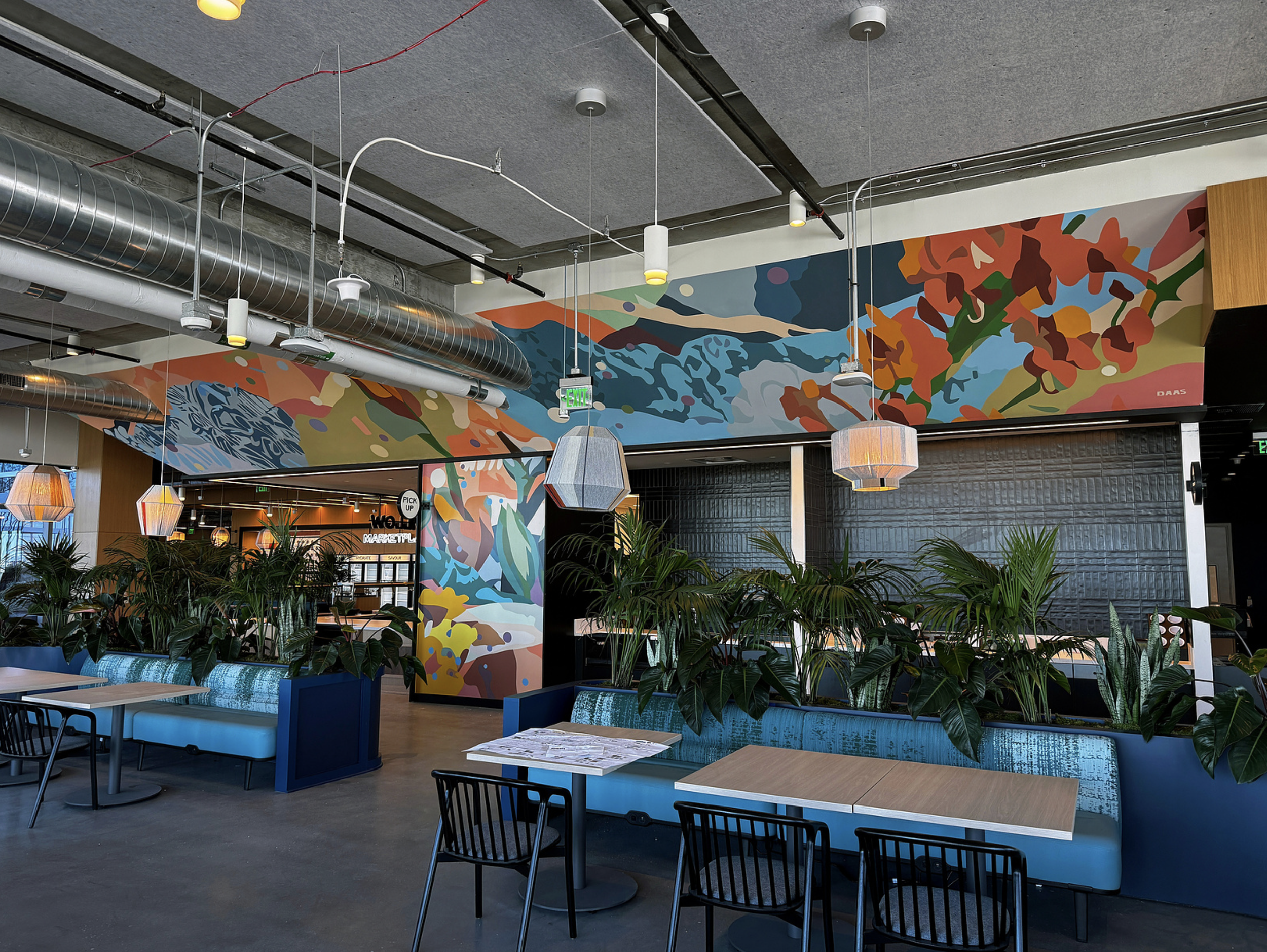 Work by the artist DAAS, Interior of a modern restaurant or cafe with colorful abstract wall murals, hanging pendant lights, potted plants, and seating with tables and chairs.