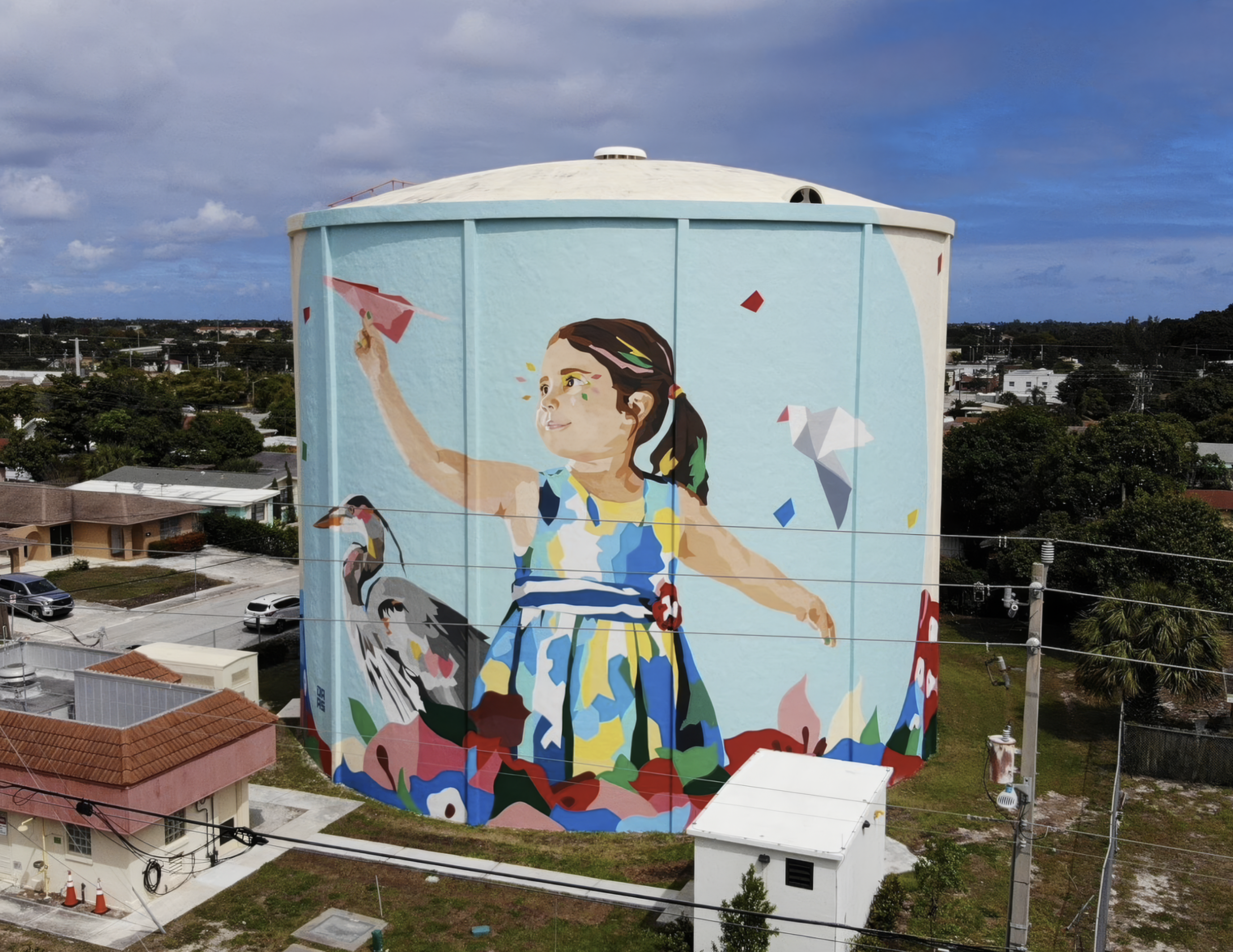 Work by the artist DAAS, A large mural painted on a water tower features a young girl with pigtails, holding a kite string, surrounded by colorful birds and abstract shapes, in a vibrant, colorful style.