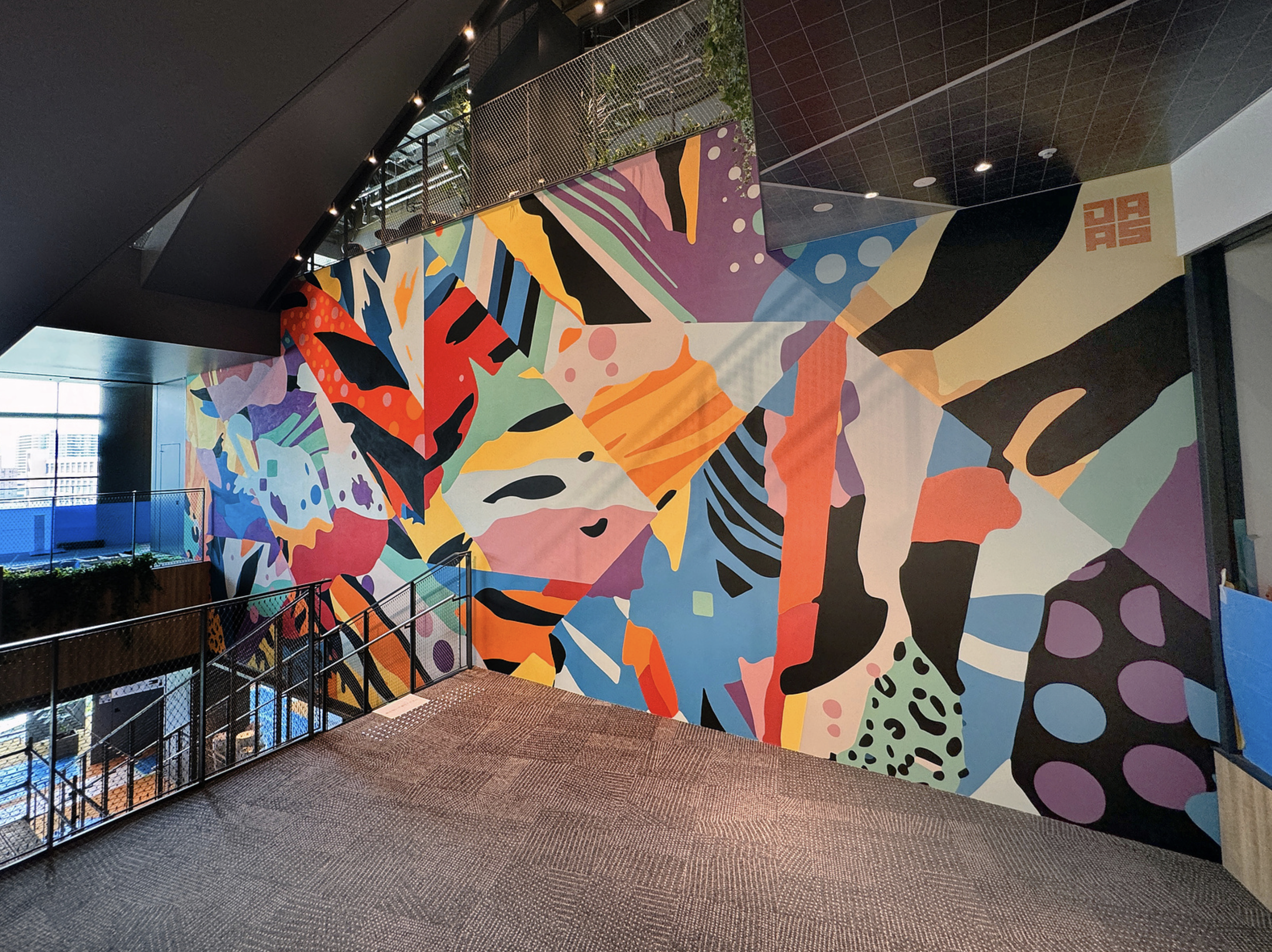 Work by the artist DAAS, Colorful abstract mural art on a large interior wall featuring various shapes and patterns in vibrant colors.