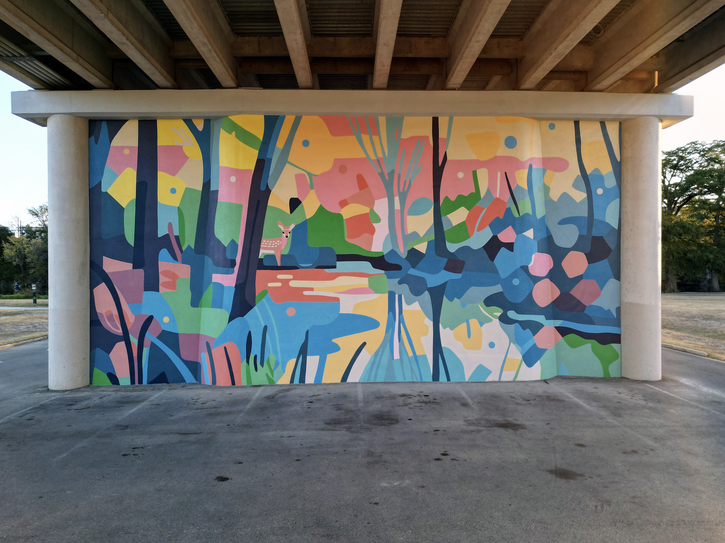 Work by the artist DAAS, Colorful abstract mural of a forest scene with trees, a deer, and a stream, painted under a bridge.