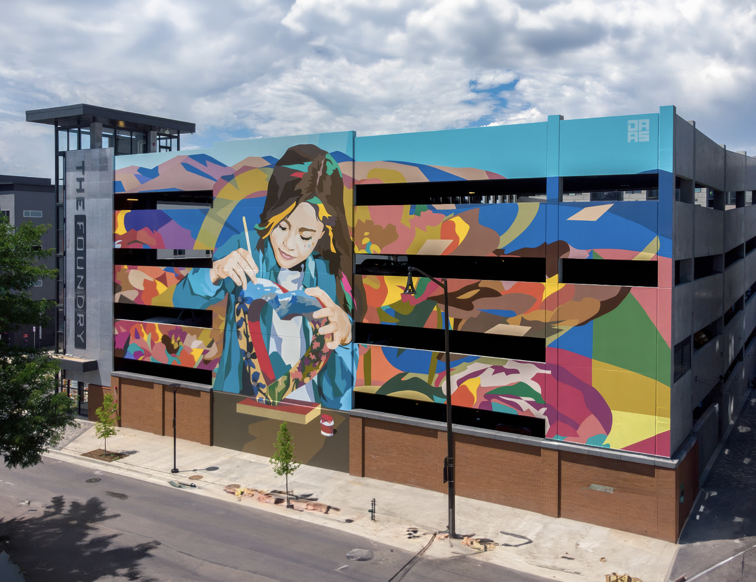 Work by the artist DAAS, Colorful mural on a building depicting a woman painting, with an abstract background and a ladder in front.