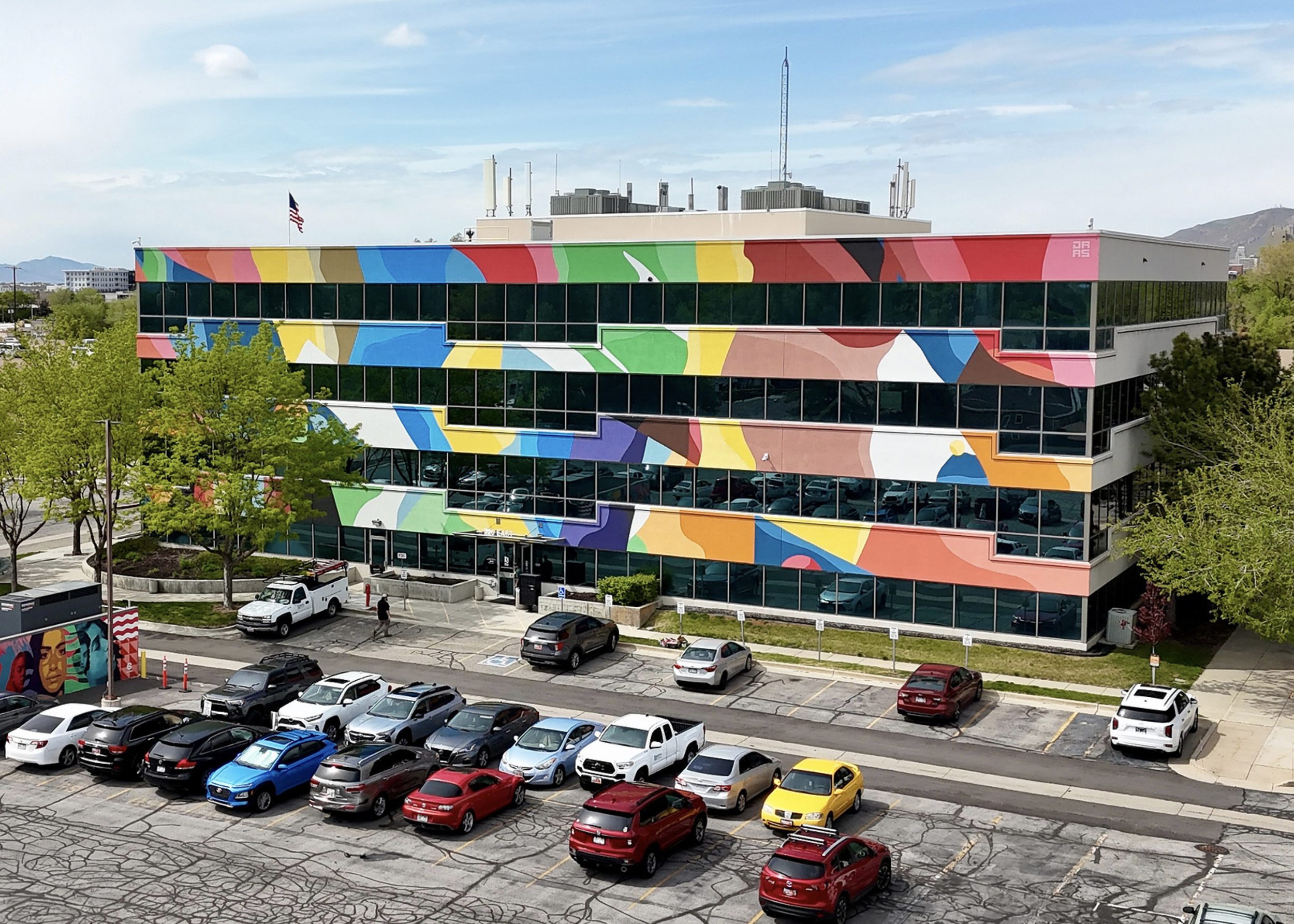 Work by the artist DAAS, Colorful mural on a modern office building with a parking lot in front.