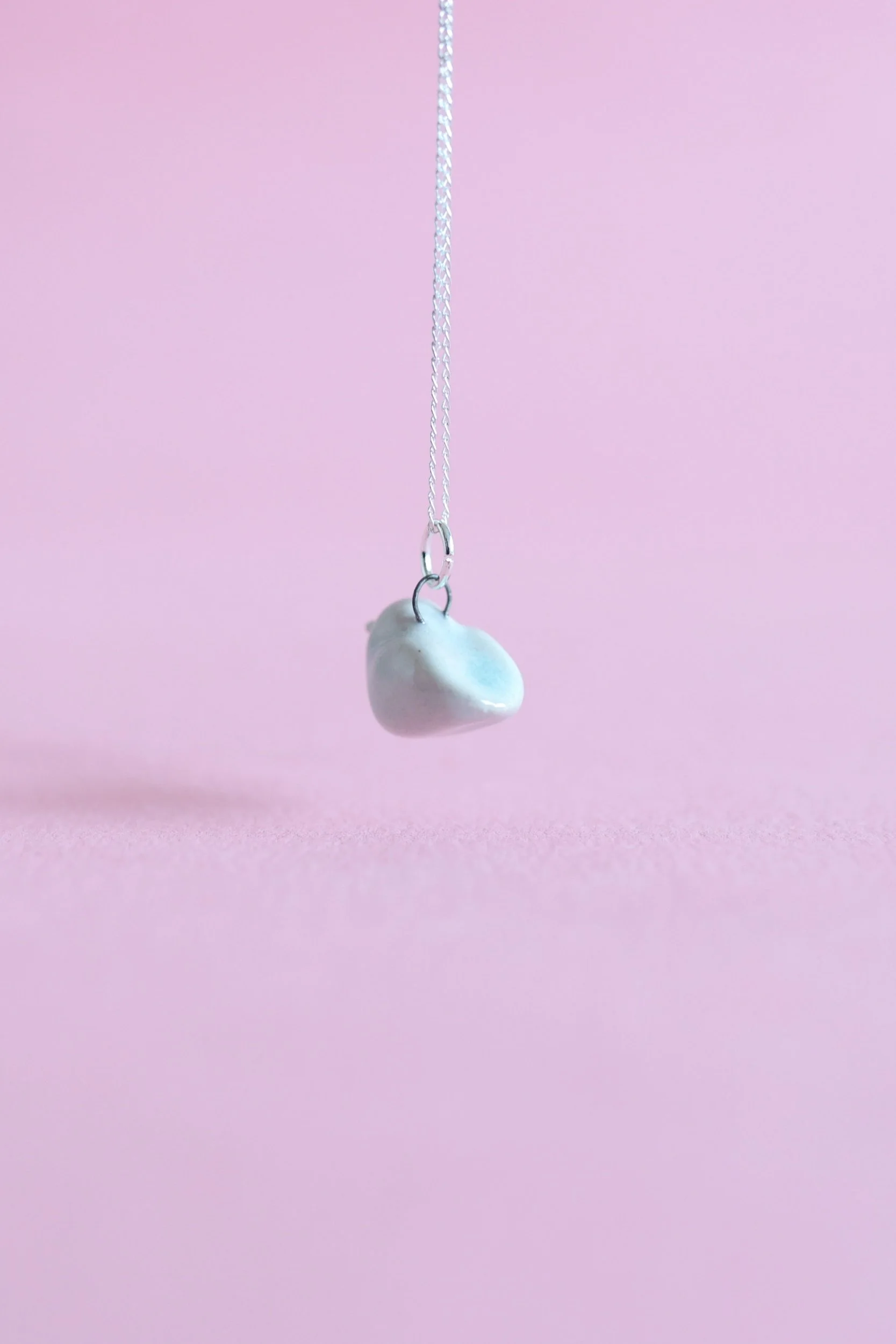 A turquoise ceramic bird is suspended in the air on a sterling silver chain in front of a pink background.