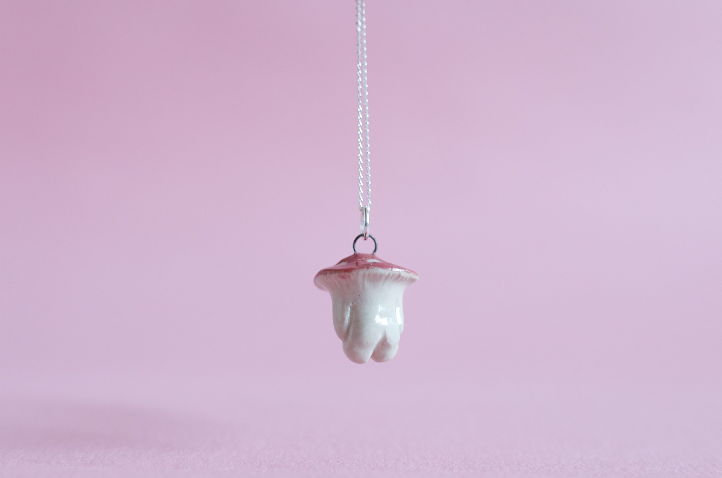 Rear view of cute kawaii inspired mushroom pendant suspended in front of a pink background.