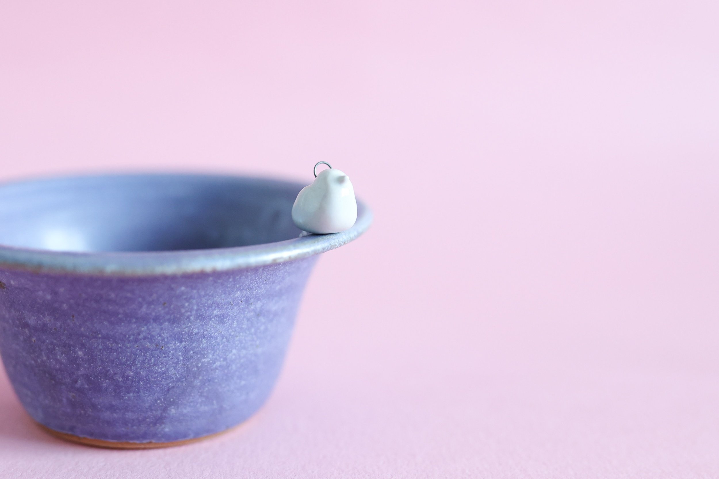 A turquoise ceramic bird sits on the edge of a purple bowl.