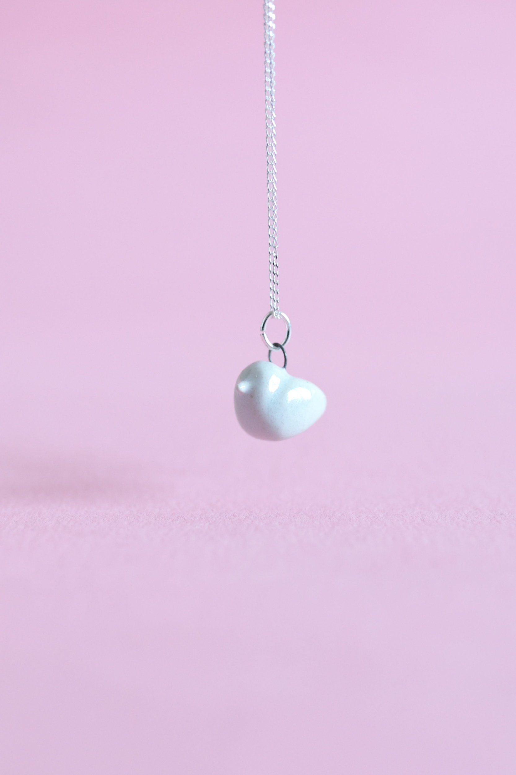 A turquoise ceramic bird is suspended in the air on a sterling silver chain.