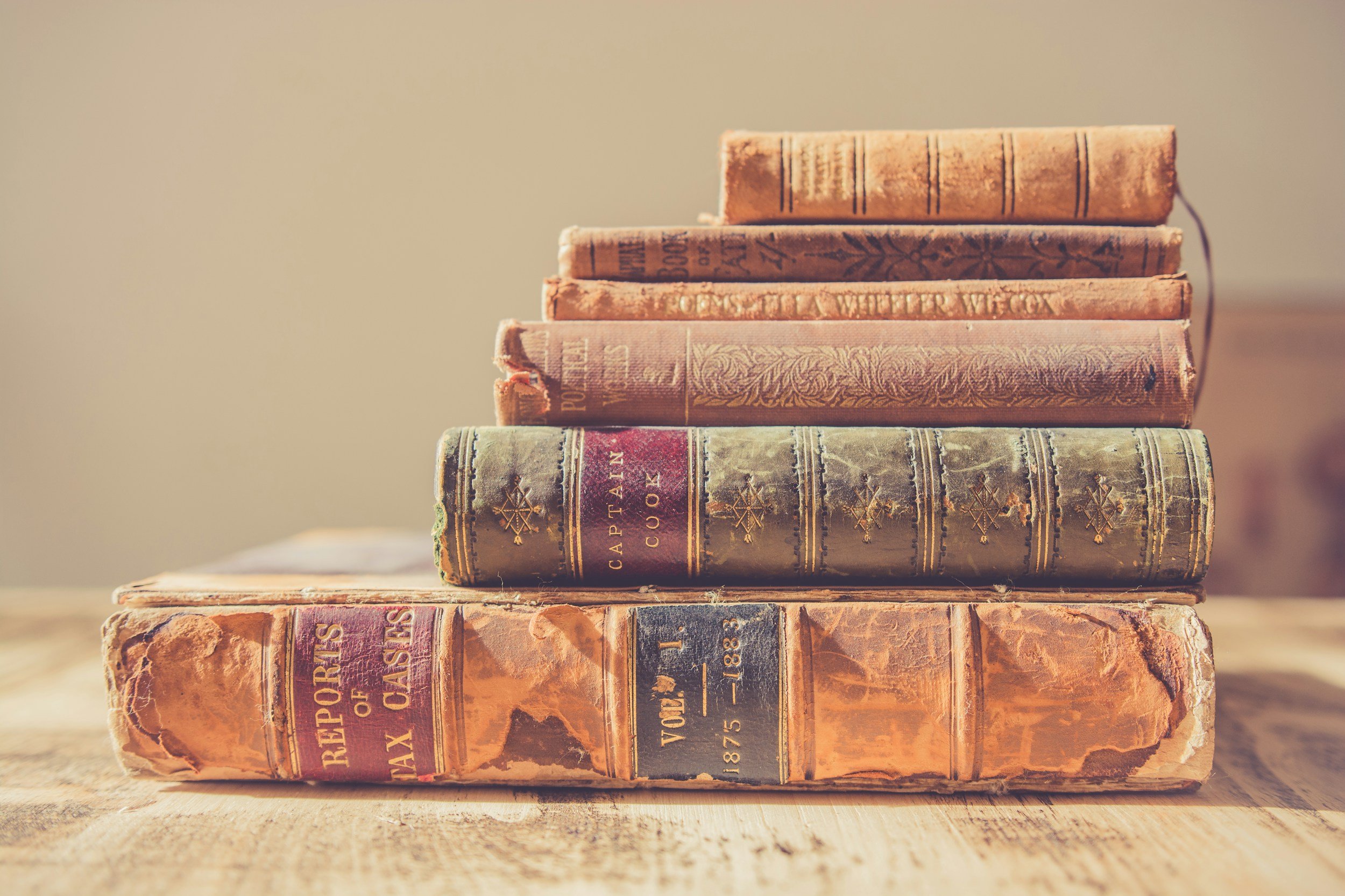 A stack of old, weathered hardcover books with worn covers and faded titles, placed on a wooden surface.