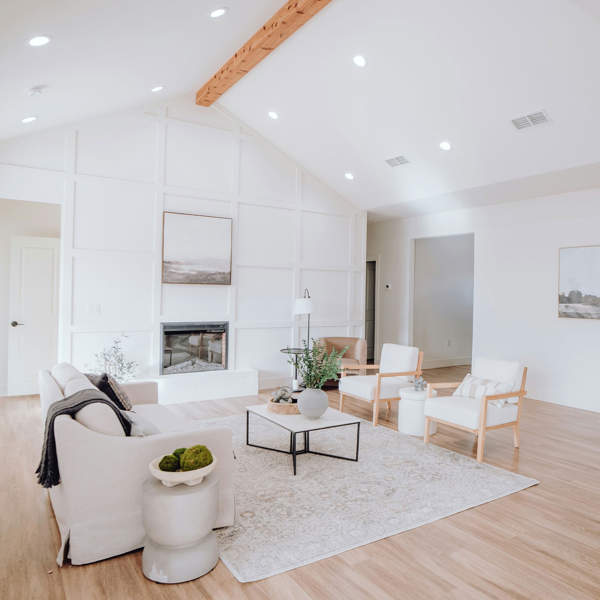 A BAM Restoration client that shows their mold-free Bright living room with white walls, wooden flooring, and modern furniture, including a sofa, armchairs, a coffee table with a potted plant, and minimal decor.