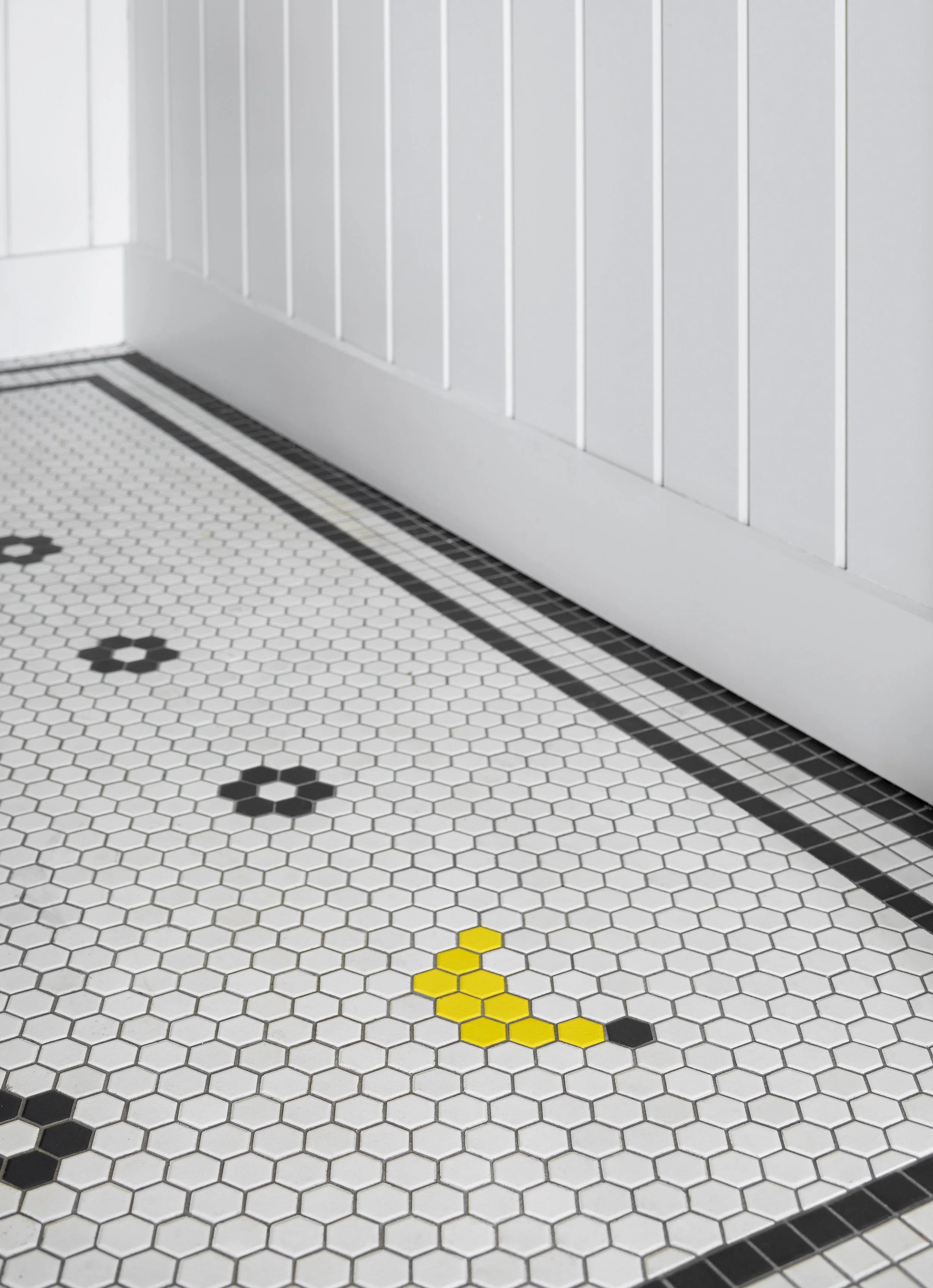 White hexagon tile floor with black and yellow accents, white beadboard wall with baseboard.