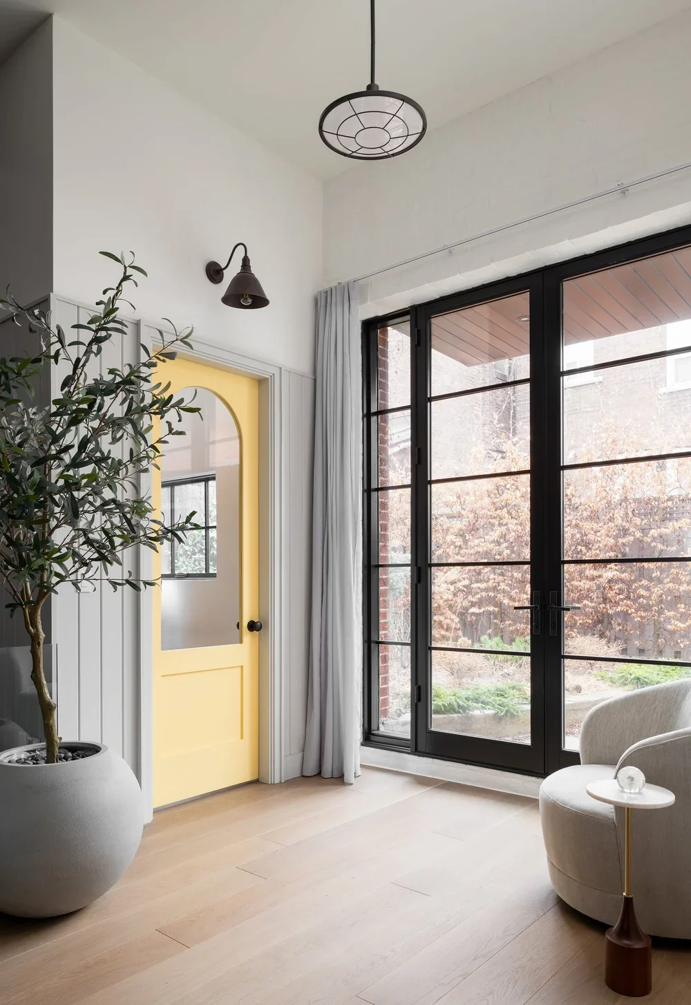 Bright living room with a large sliding glass door, a potted plant, a yellow door with a mirror, and a cozy armchair.