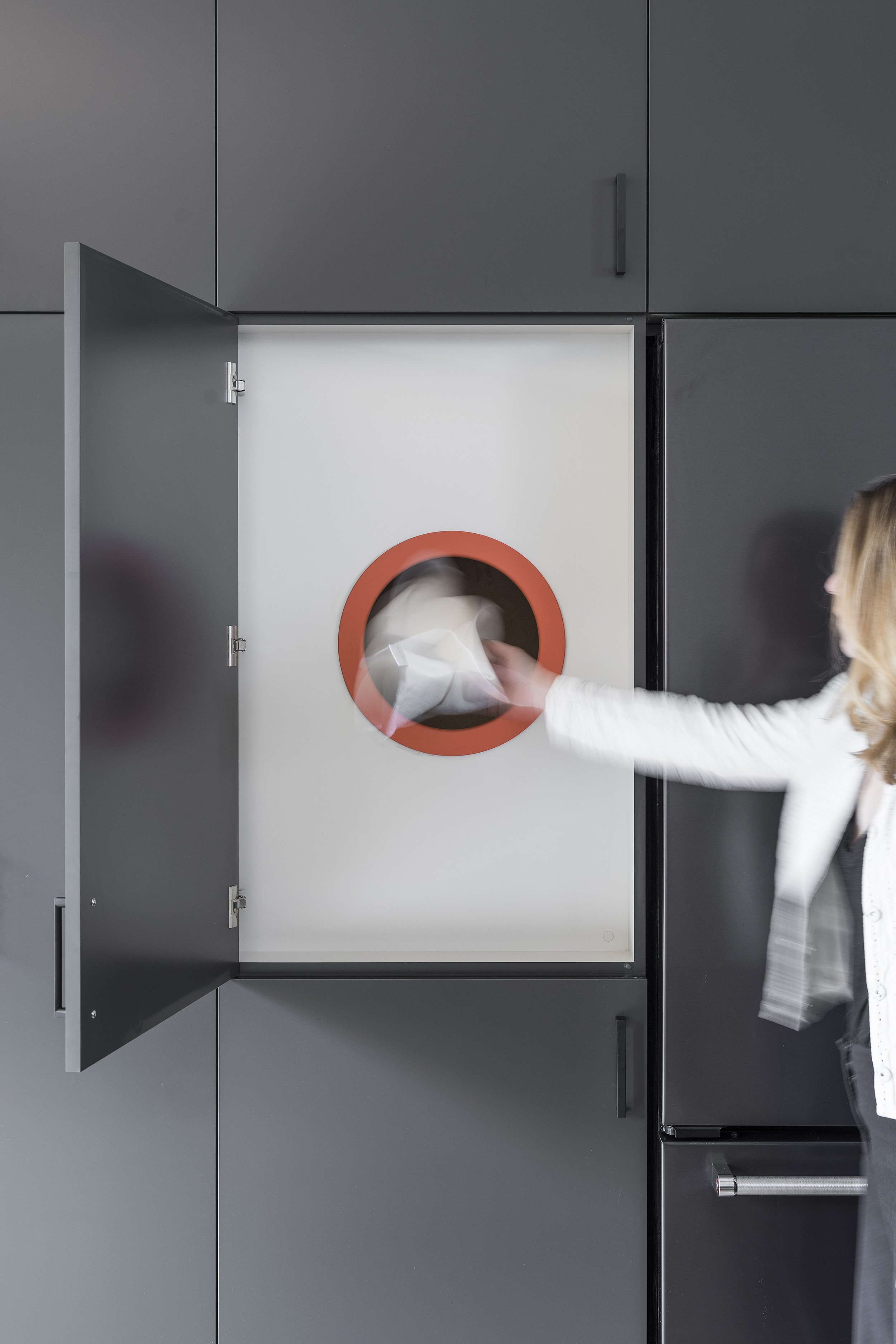 A person is putting laundry into a front-loading washing machine in a laundry room with gray cabinets.