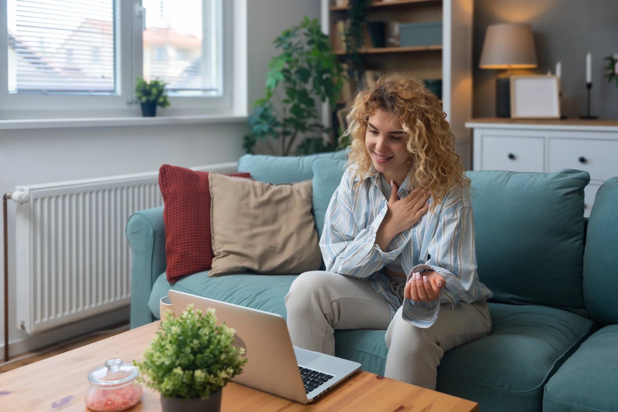 Woman seated on a sofa at home with a laptop on the table in front of her.