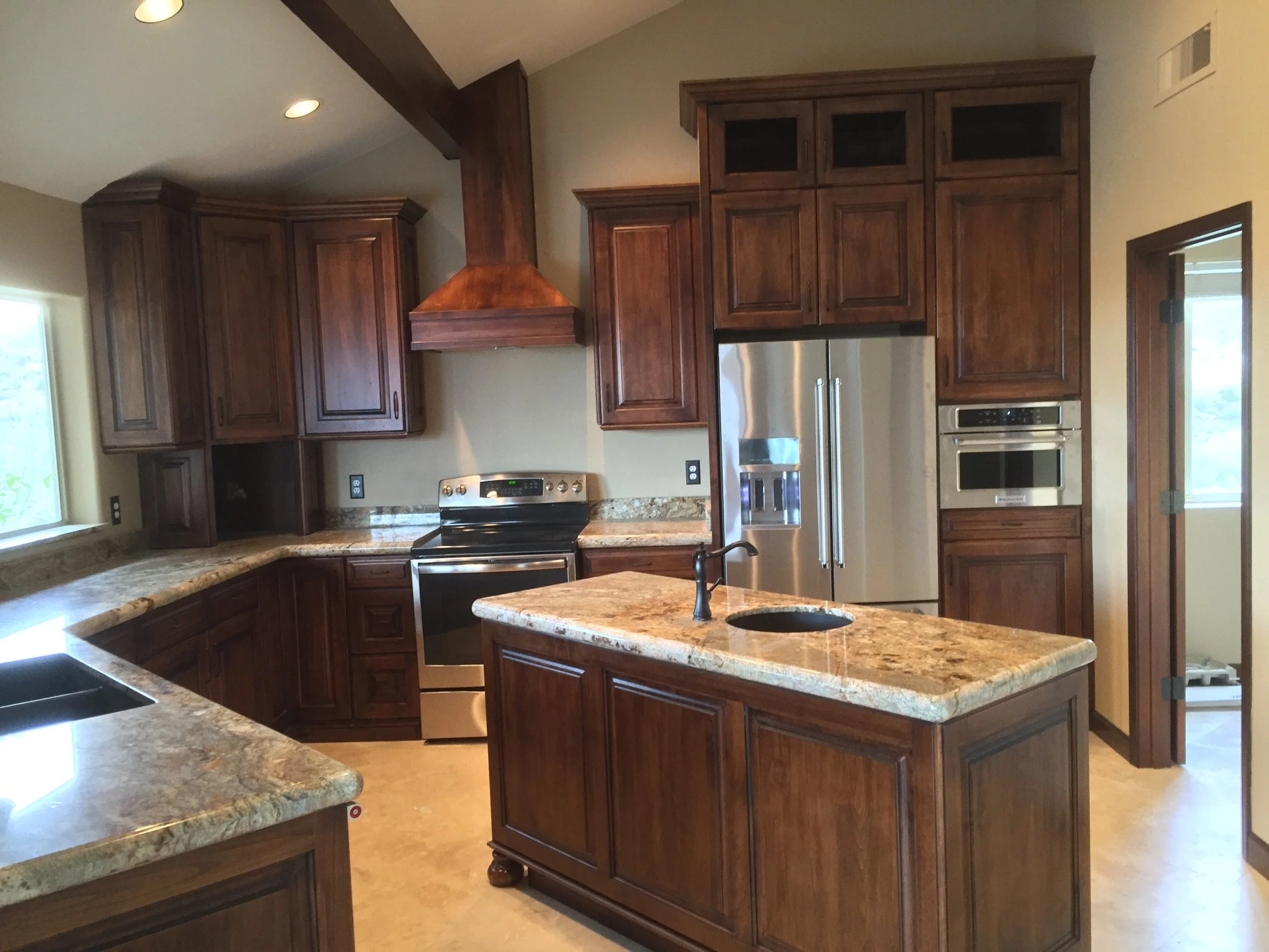 A kitchen with wooden cabinets, granite countertops, stainless steel appliances, and a kitchen island with a small sink.