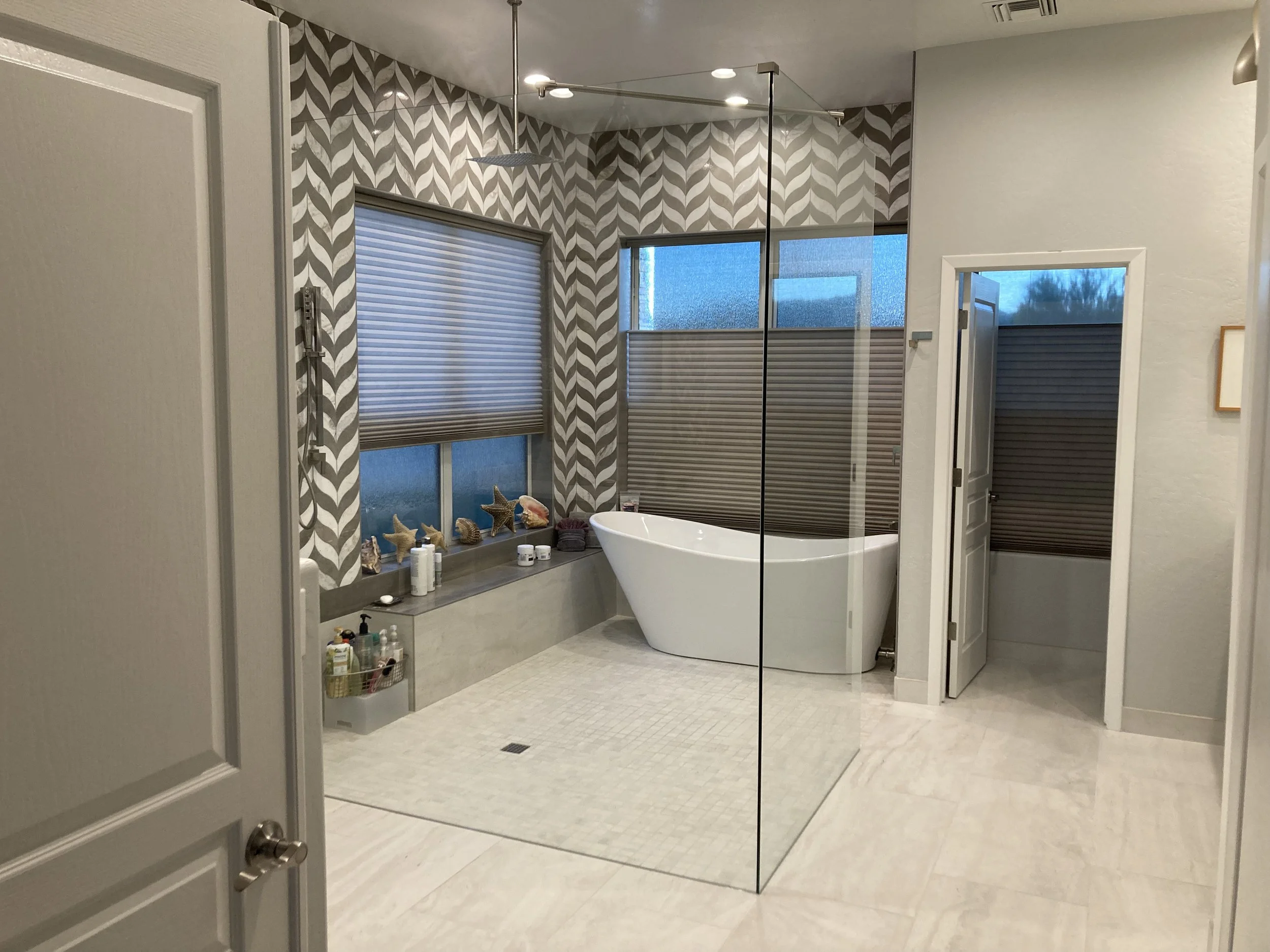 Modern bathroom with a free-standing bathtub, large windows with patterned blinds, seashell decorations, and a glass shower enclosure.