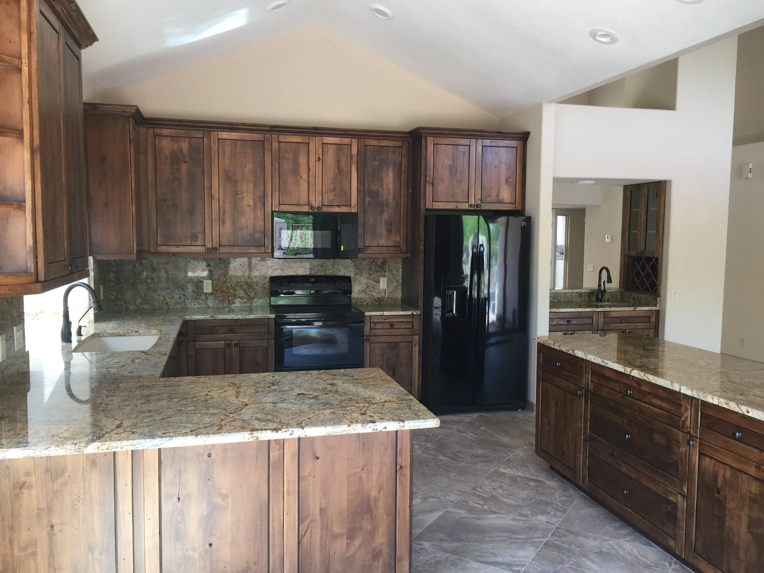 Kitchen with wooden cabinets, granite countertops, black appliances including a refrigerator and microwave, and a tiled floor.