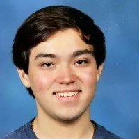 Portrait of a young man with dark hair and a friendly smile, wearing a blue shirt, against a blue background.
