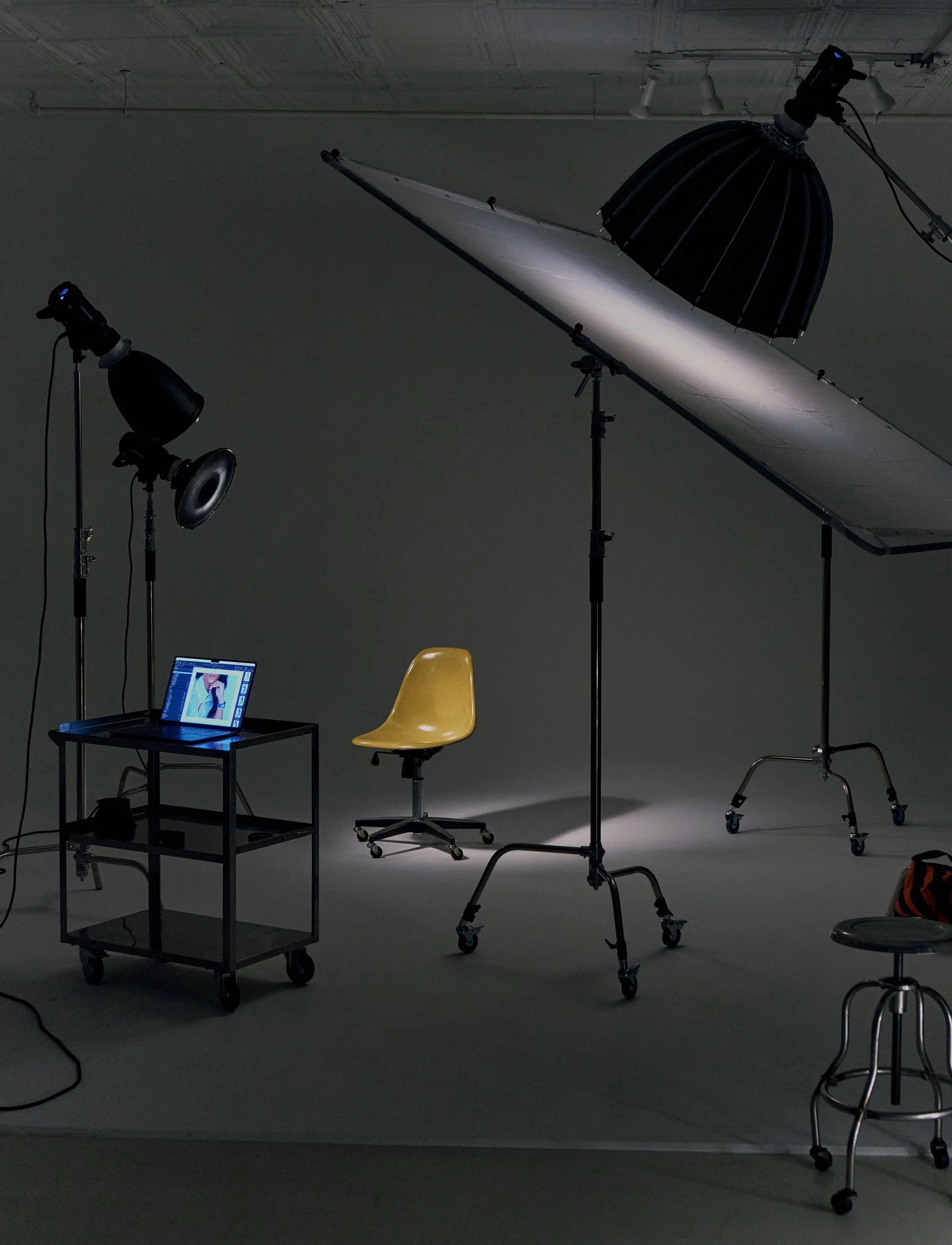 Photography studio setup with a brown chair, a small table with a laptop, studio lights, umbrella reflectors, and a backdrop, arranged for photoshoot.
