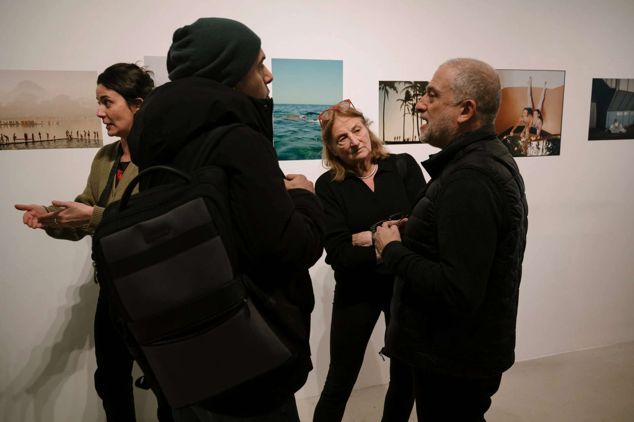 Group of four people having a conversation at an art gallery exhibition, with photographs of nature on the wall behind them.