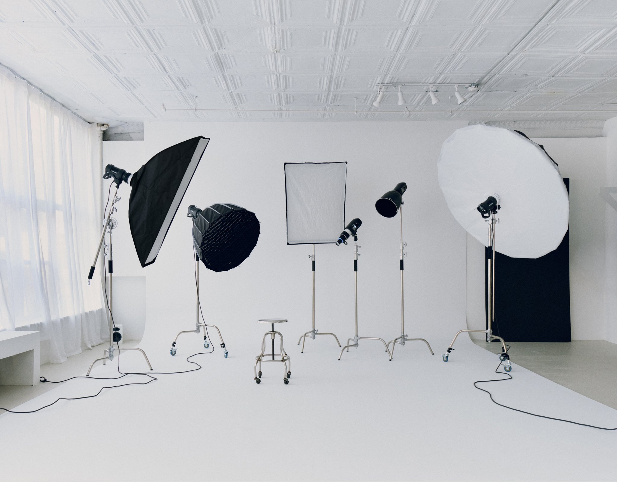 Photography studio setup with various professional lighting equipment and backdrop on a white floor and wall.