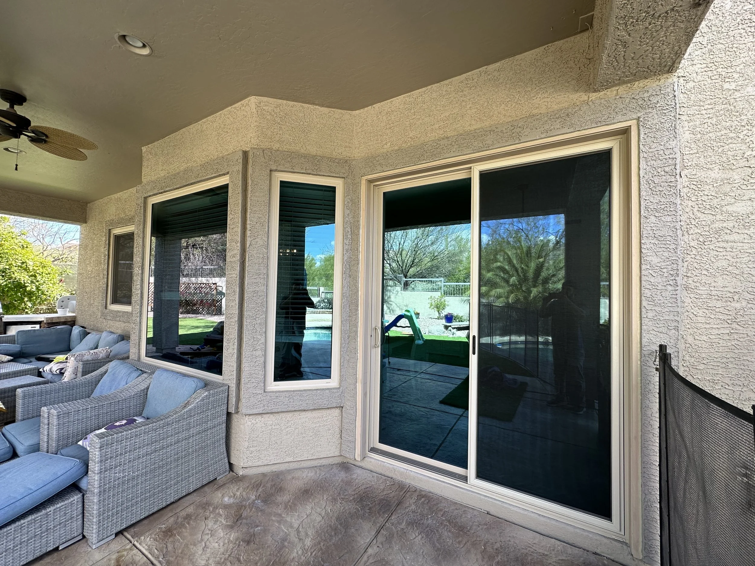 Patio area with wicker and cushioned outdoor furniture, a sliding glass door, windows, and a screened-in porch with a view of a backyard pool and greenery.
